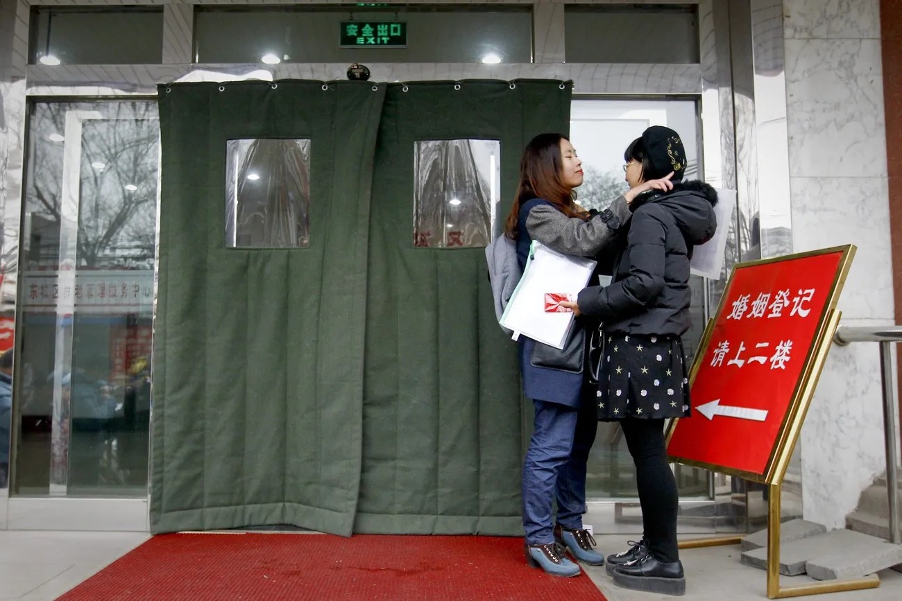 北京某婚姻登記處門口一幕：她們原本想在這裡登記結婚，但遭到拒絕。其實她們並非情侶，但她們明知自己會被拒絕結婚，卻仍希望藉此喚起人們對中國LGBT群體困境的關注，他們面臨著歧視，缺乏社會福利。