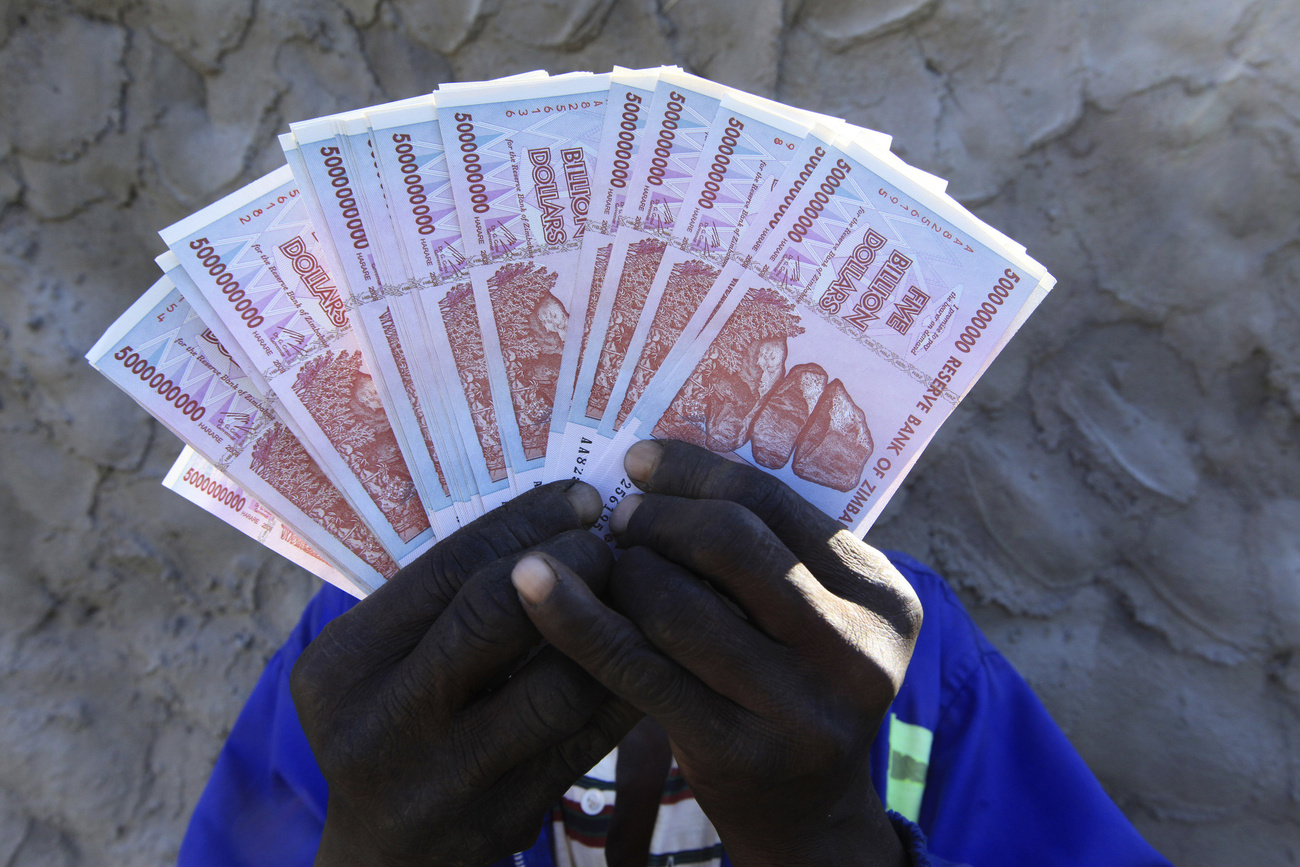 uomo mostra banconote di dollari dello zimbabwe del valore di 5 milairdi ciascuna