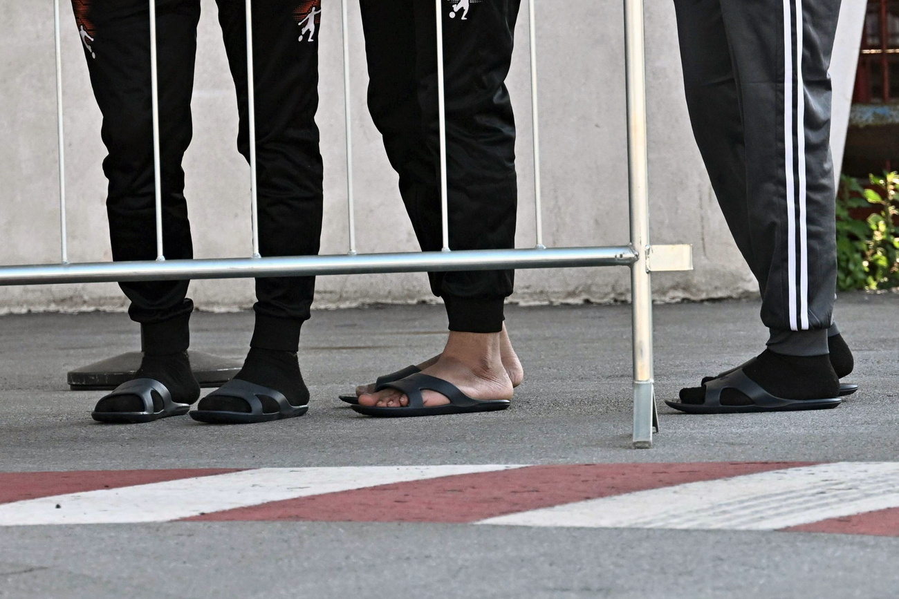 piedi di migranti in fila dietro un'inferriata