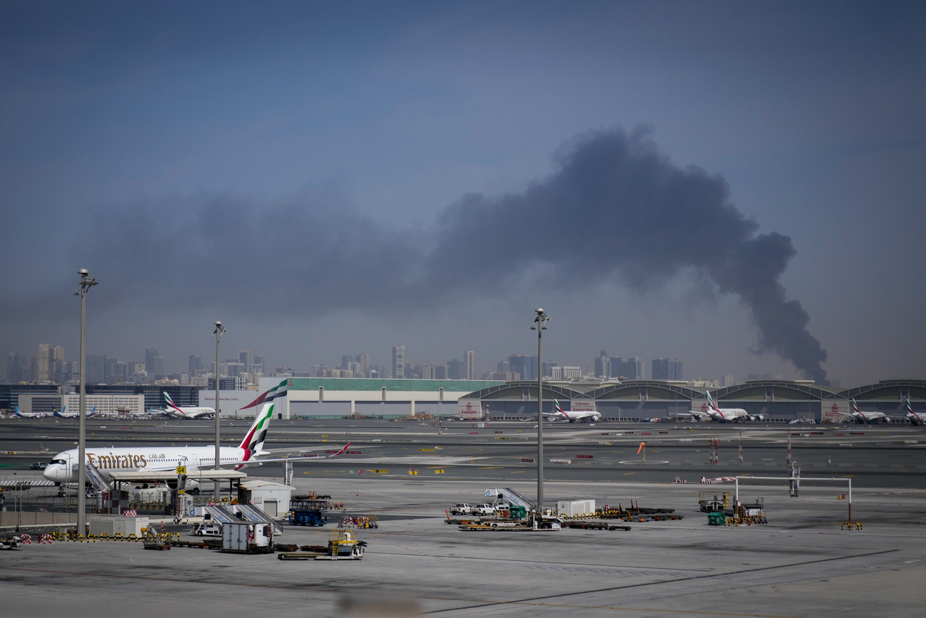 Una colonna di fumo causata da un attacco iraniano è visibile sullo sfondo, mentre gli aerei sono parcheggiati all'aeroporto internazionale di Dubai dopo la sua chiusura domenica.