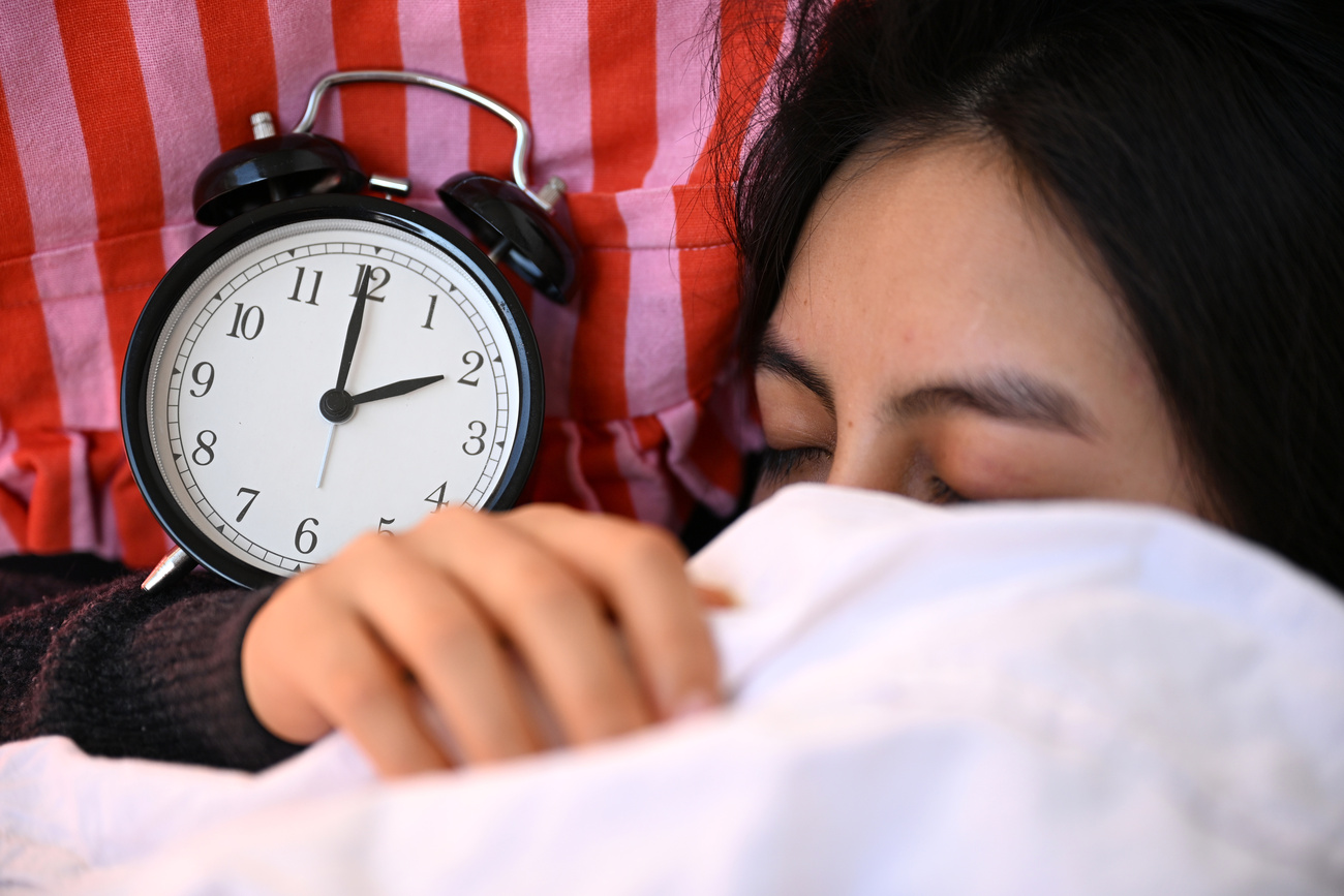 persona a letto con sveglia vicino all'orecchio