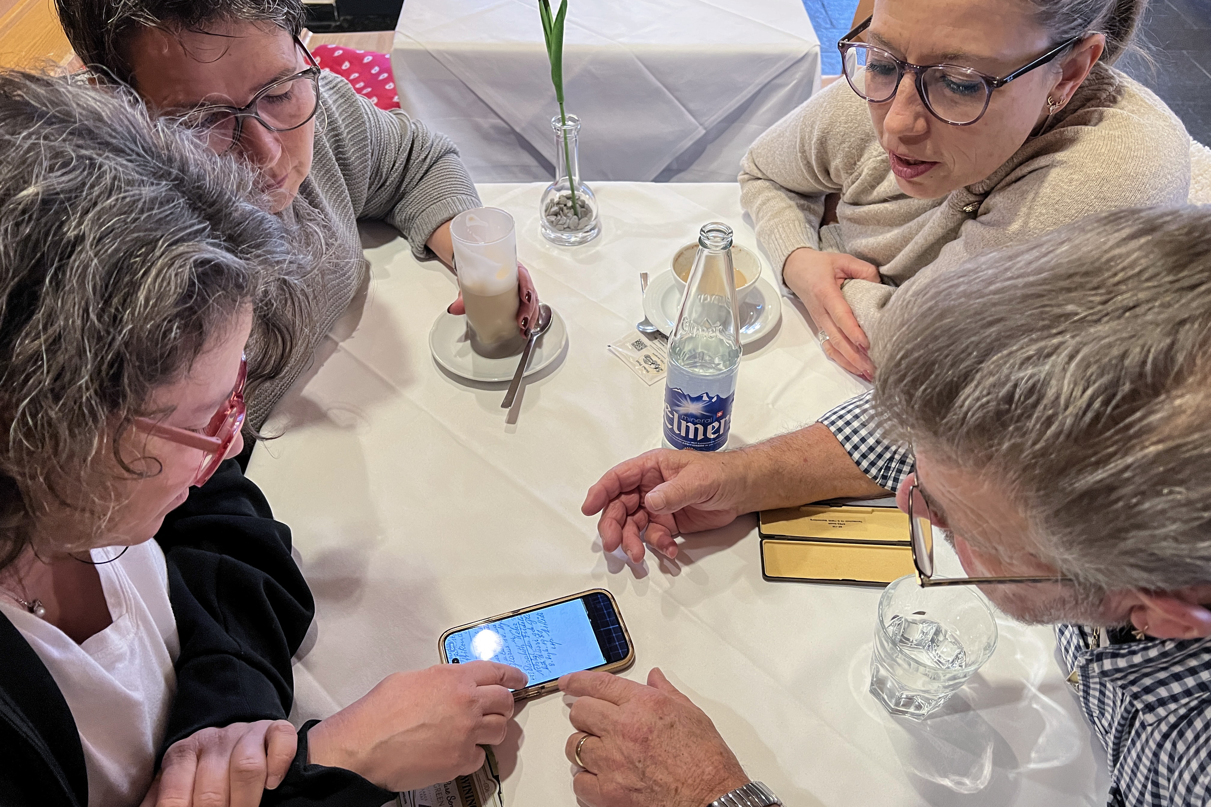 3 women and a man sitting at a table checking on a phone.