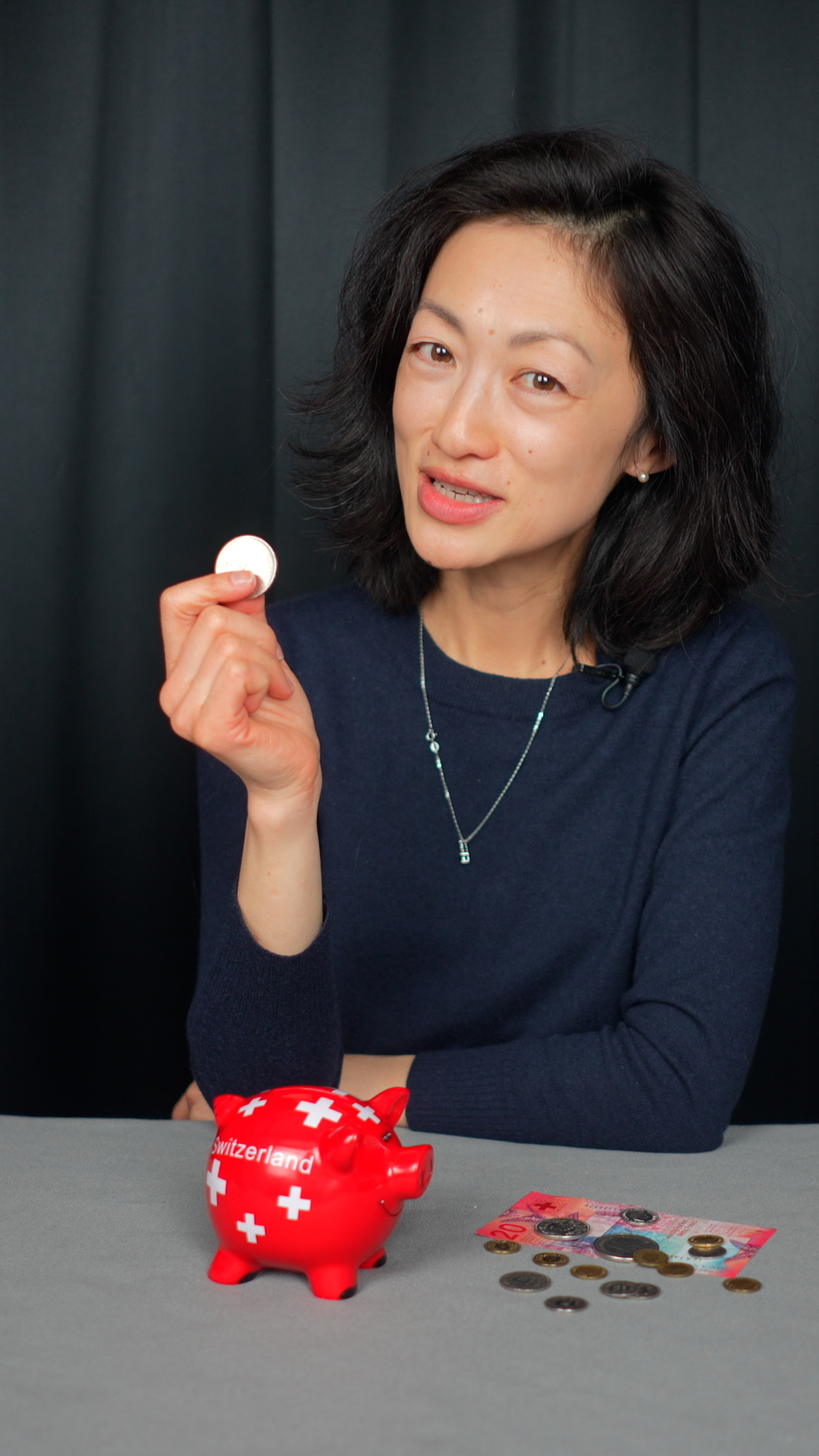 Photo of a woman holding a coin with a red piggy bank in front of her.