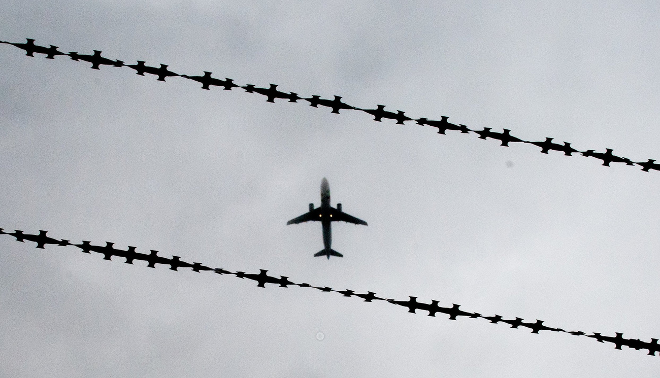 A shot of an aeroplane from below, with barbed wire in the background
