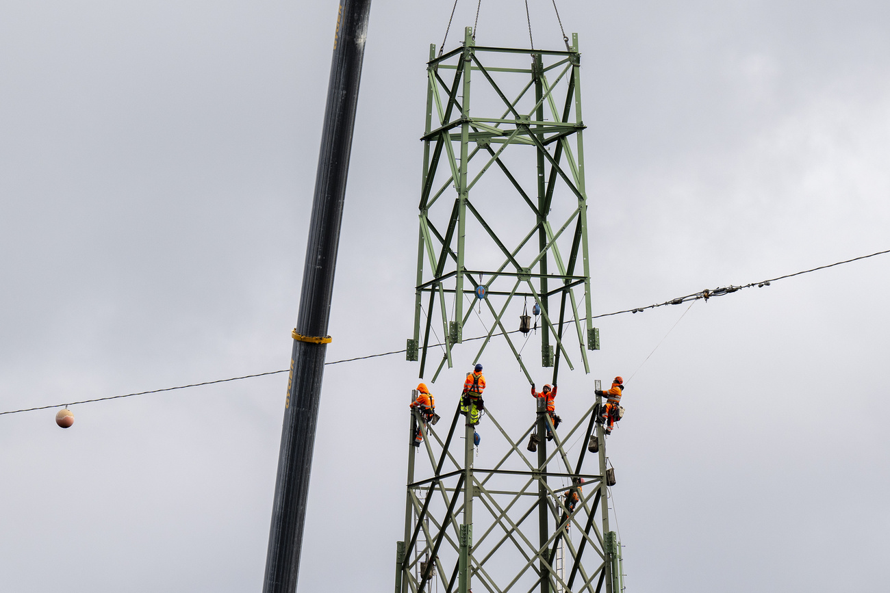Workers in orange are securing a component during construction work on the high-voltage power line