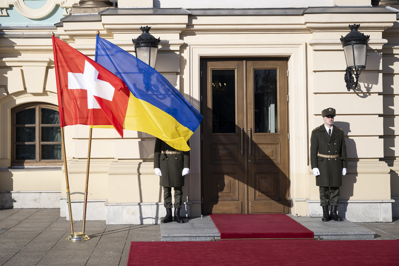 Zwei Soldaten bewachen ein Gebäude, vor ihnen die Flaggen der Ukraine und der Schweiz