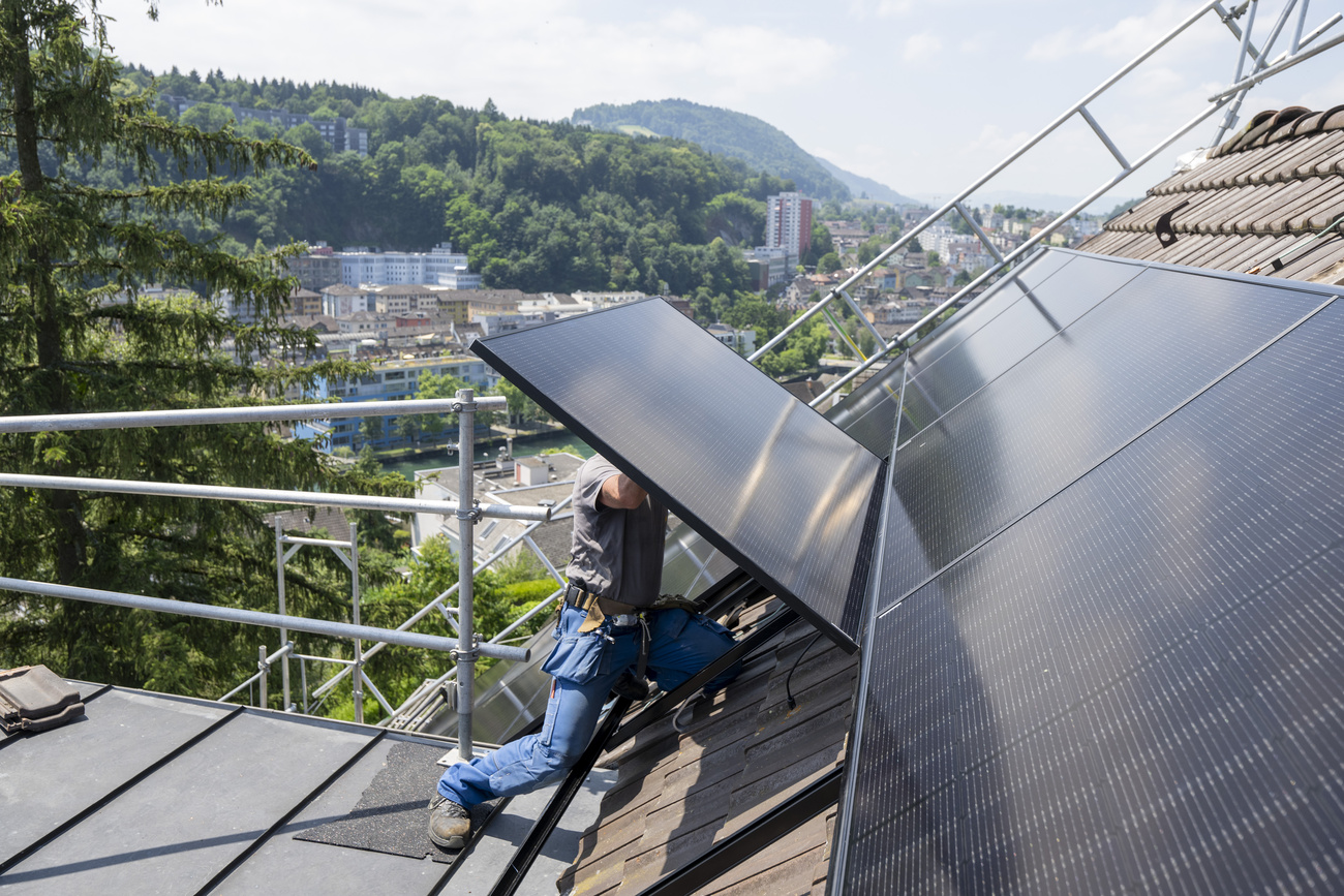 Worker installing solar panels on the roof of a residential house in Lucerne, Switzerland.