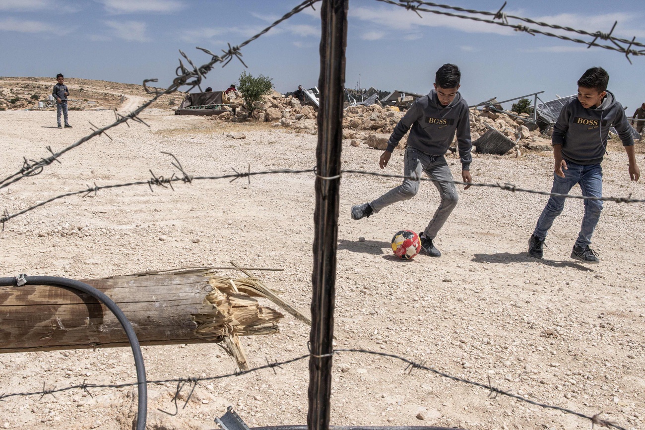 Boys playing football/soccer near damaged housing in occupied West Bank.