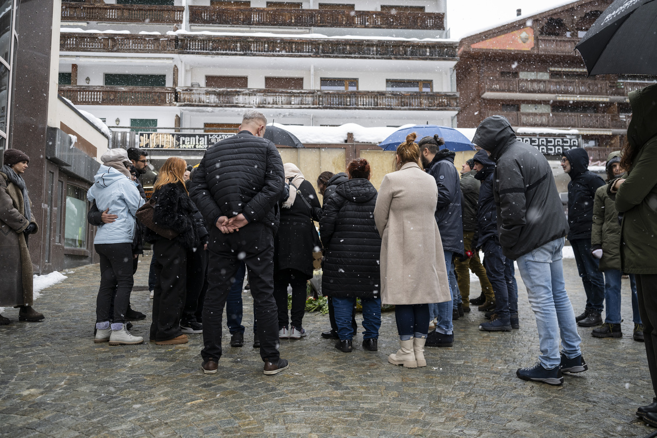 Persone in raccoglimento silenzioso davanti al bar "Le Constellation" a Crans-Montana, dove una stellina scintillante ha innescato il fatale incendio nella notte di Capodanno.