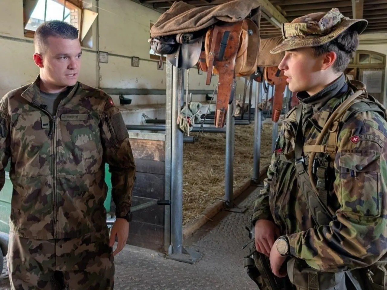 Two people in military uniform are standing in a stable