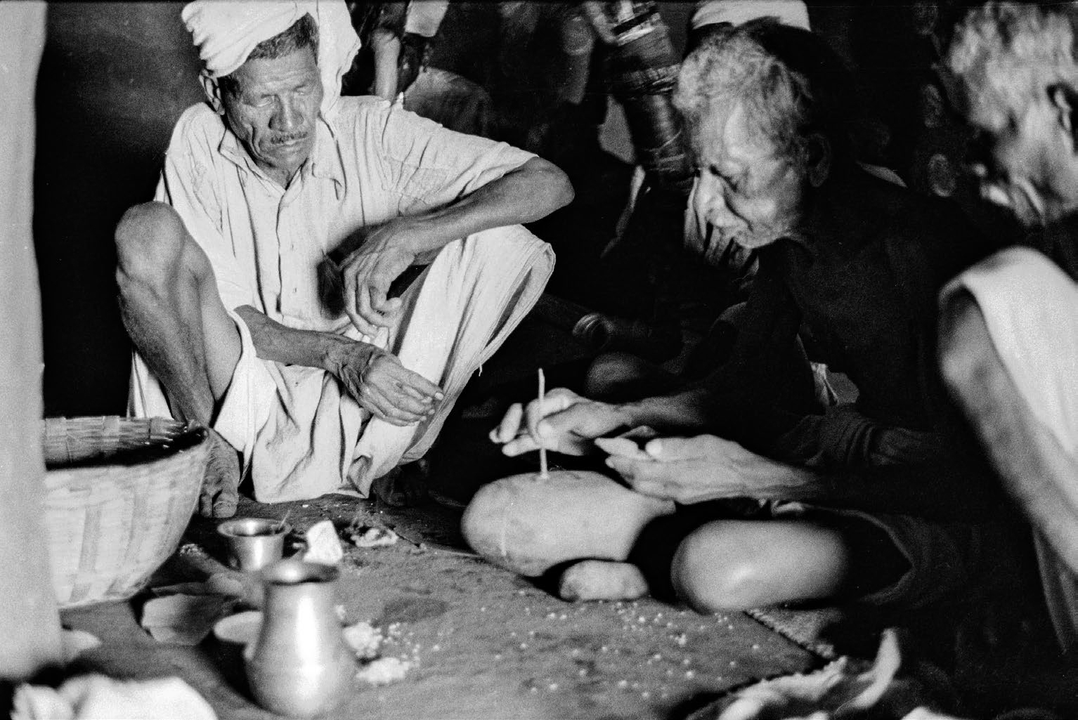A black-and-white photograph of a group of men sitting on the ground