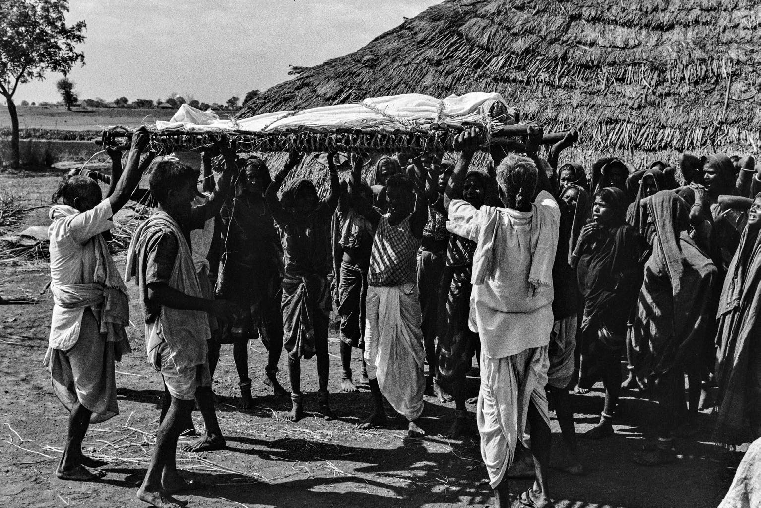 A black-and-white photograph of a group of people carrying a stretcher above their heads