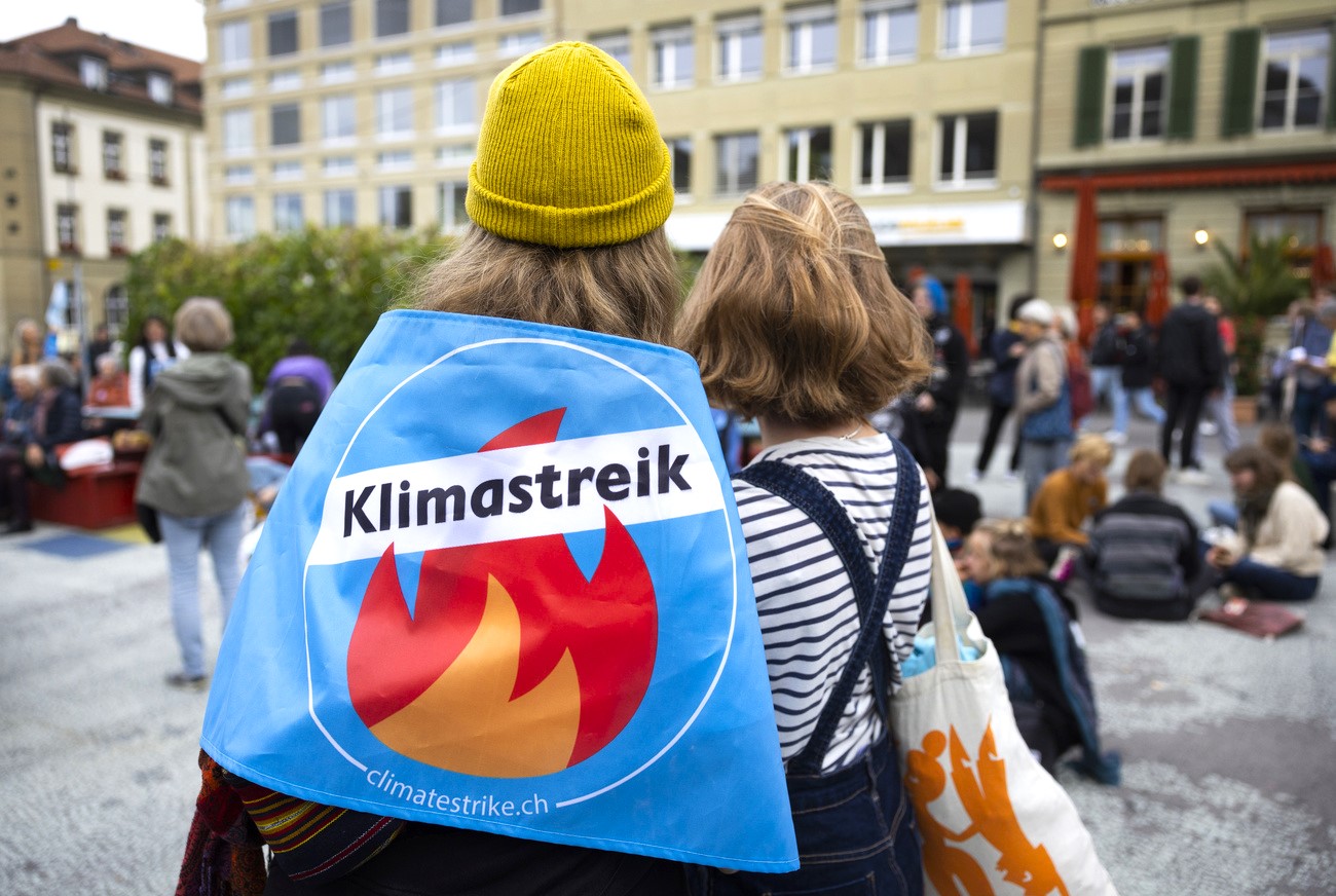 due persone con una bandiera dello sciopero per clima sulle spalle sono in piedi in mezzo a una piazza