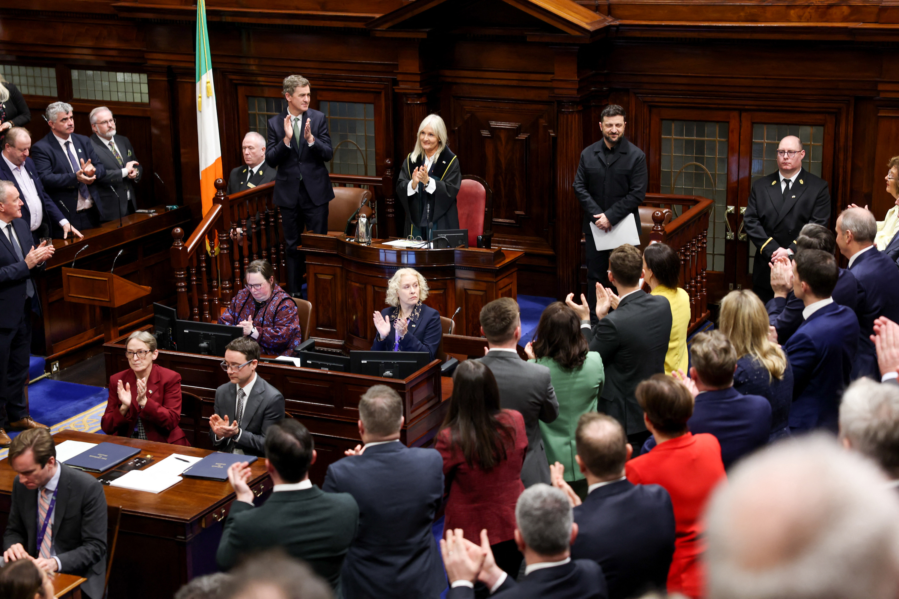 People clapping in the parliament chamber and an Irish flag can be seen