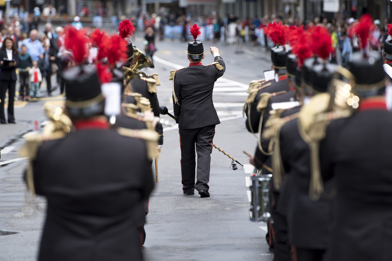 Musikanten marschieren die Strasse hinunter, angeführt von einem Dirigenten, der den Taktstock hebt