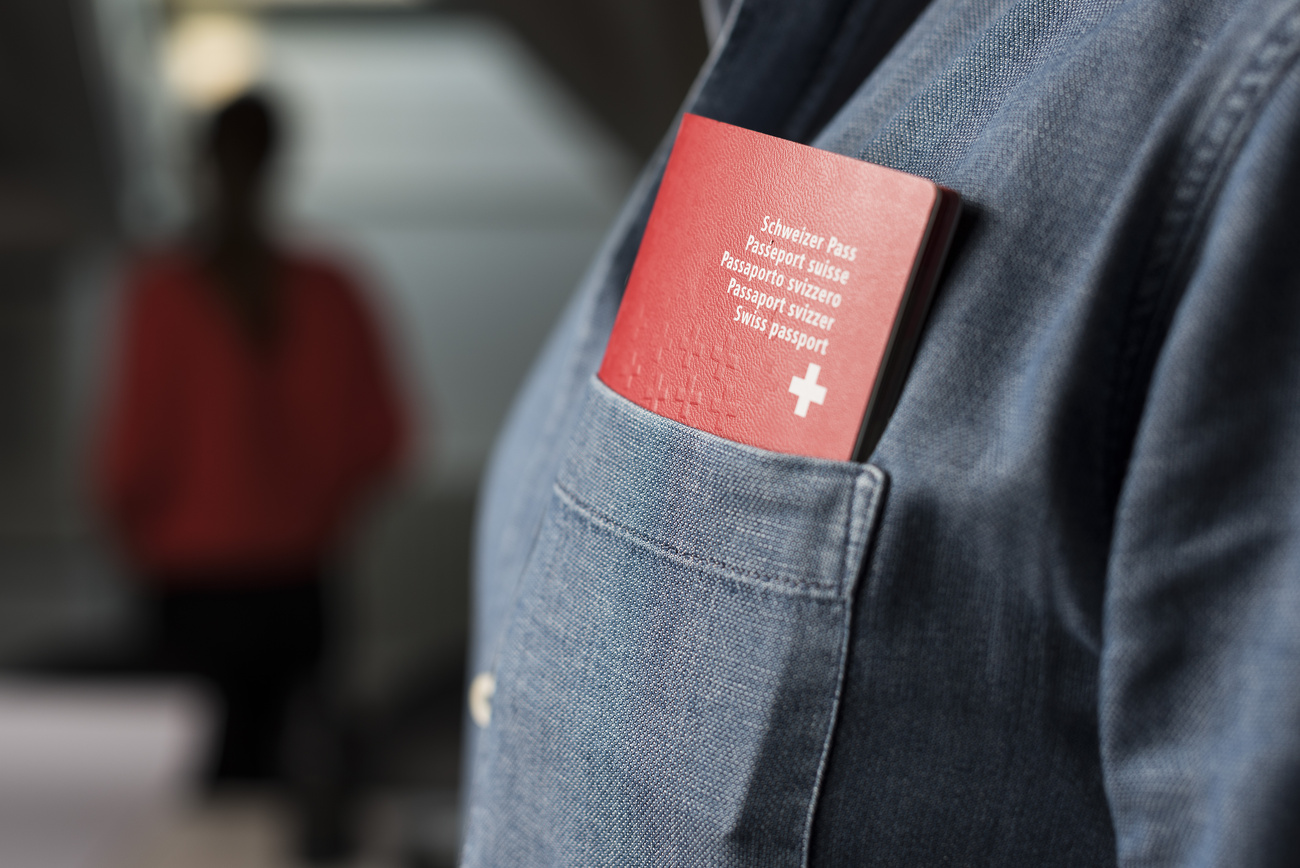 Part of a Swiss passport can be seen in a shirt pocket; a blurred figure can be made out in the background