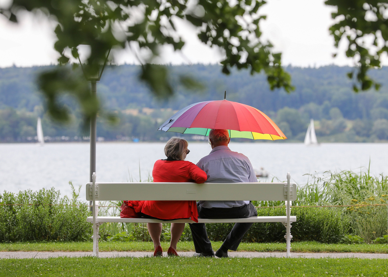 Ein älteres Paar sitzt unter einem Regenschirm auf einer Bank
