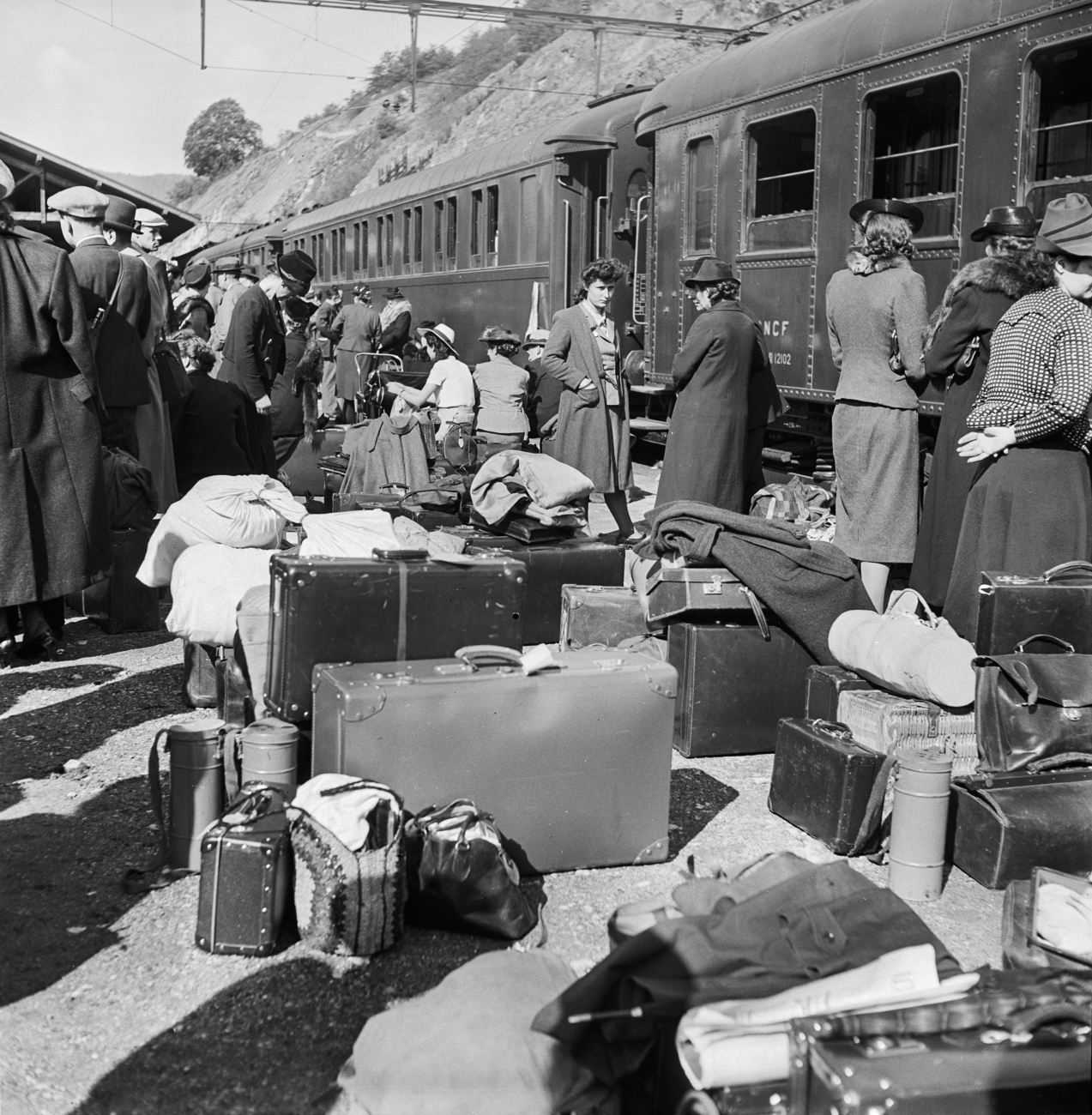 Grupo de desempregados suíços que emigra para o Brasil espera numa estação ferroviária na Suíça pelo comboio que os levará aos portos marítimos.