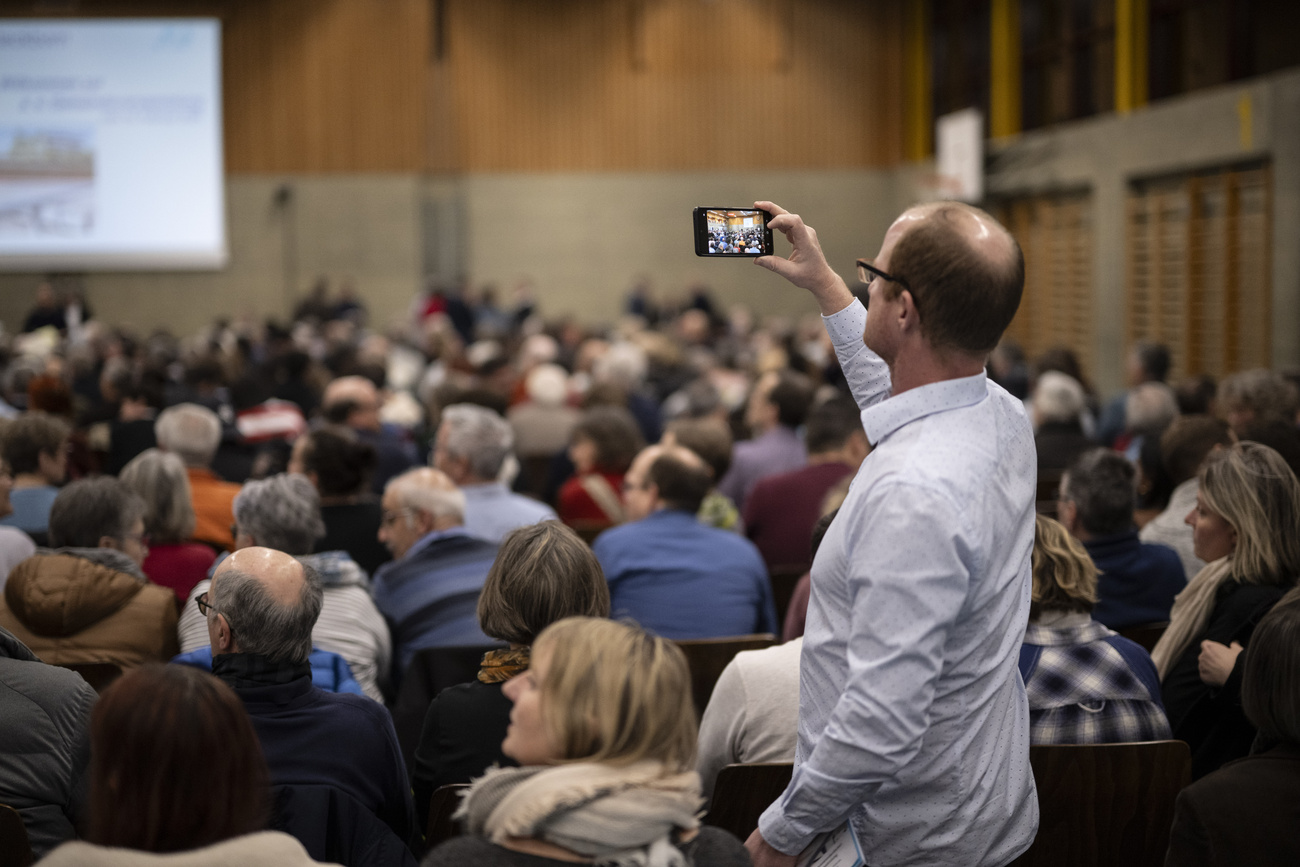 uomo fa una foto con il telefono durante un'assemblea comunale