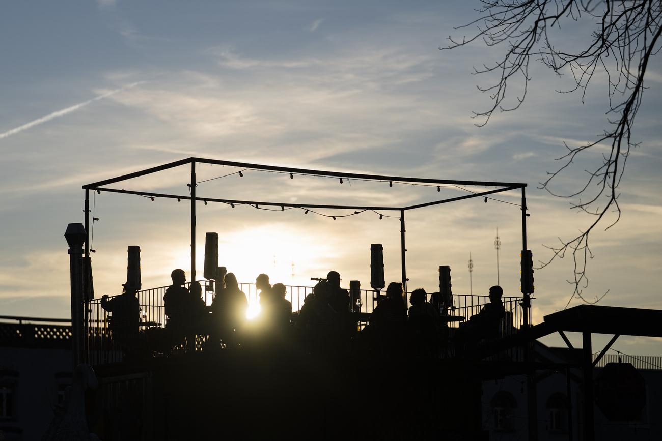 The silhouettes of people on a rooftop terrace at sunset