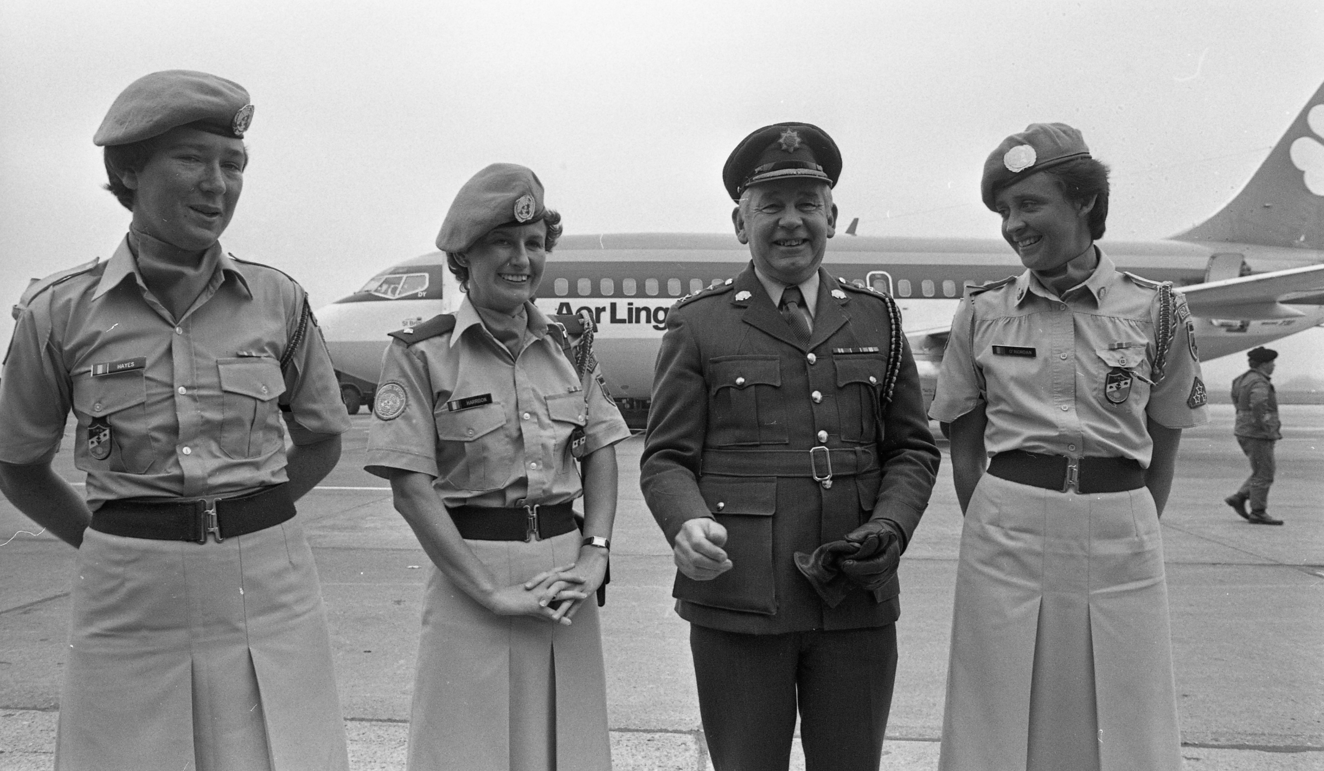Black-and-white photo of three female soldiers and one male officer standing on an airport tarmac with an Aer Lingus airplane in the background.