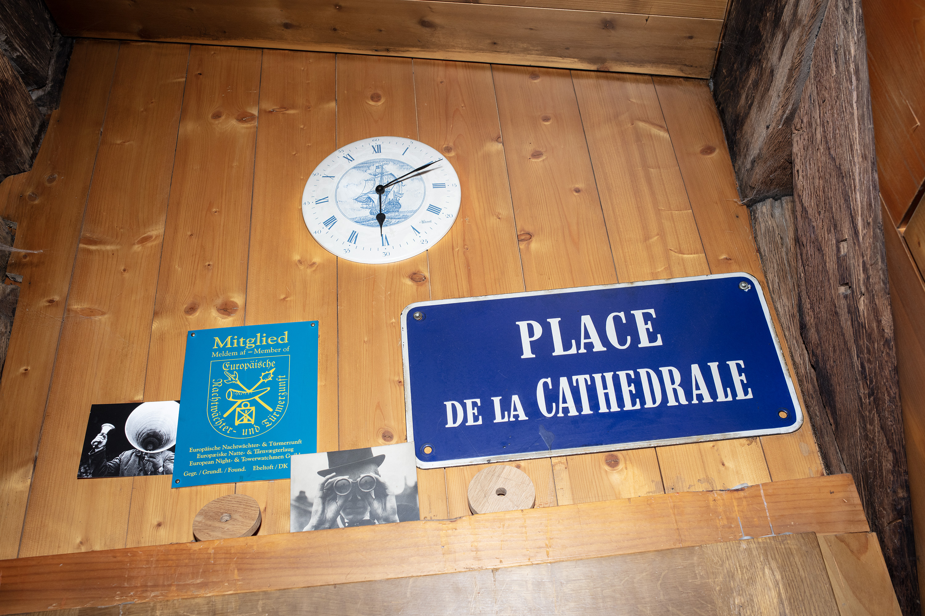 Ein Emailschild "Place de la Cathedrale" und eine Wanduhr hängen an einer vertäfelten Wand