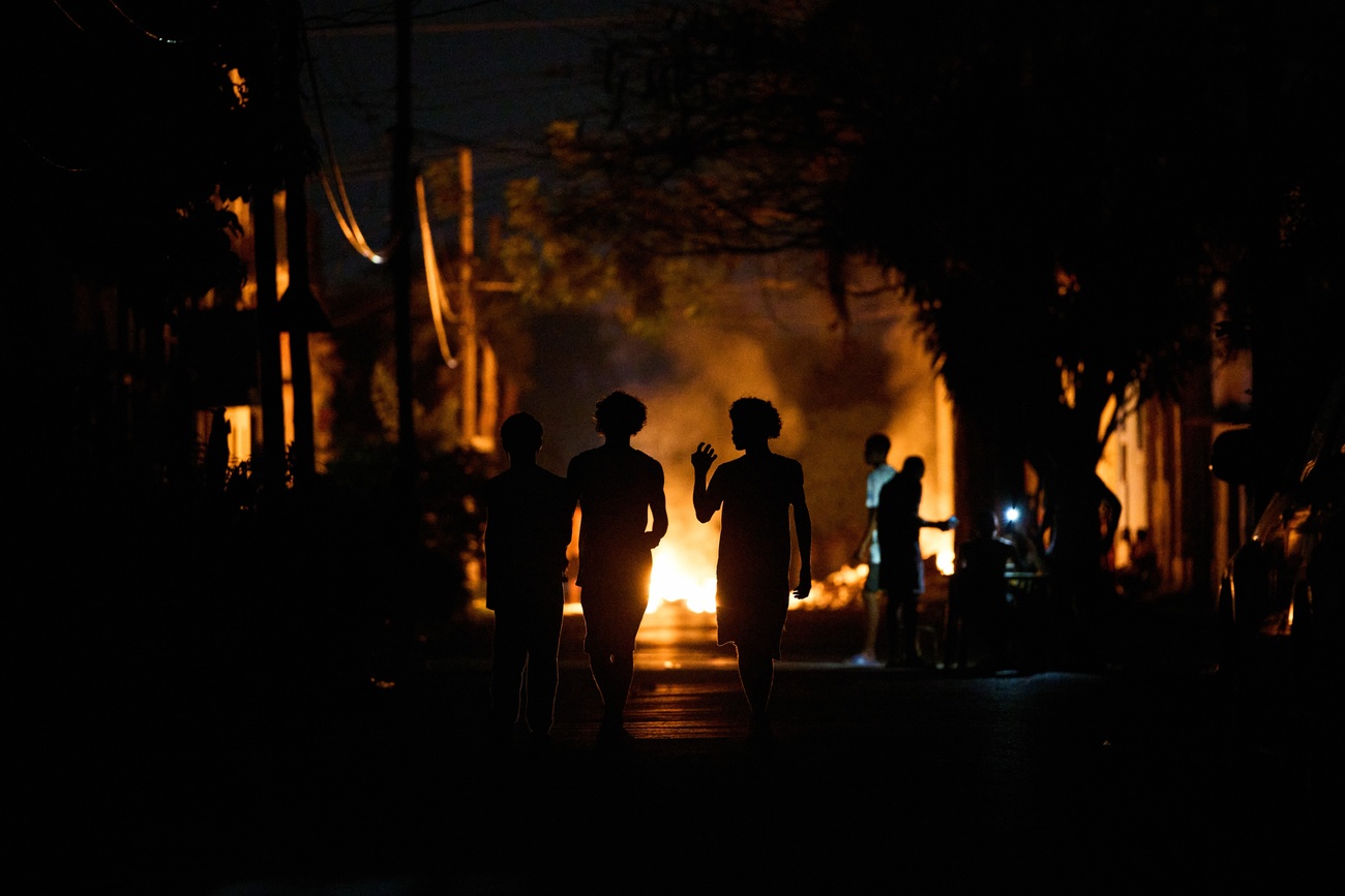 Personas caminan por la calle junto a una hoguera encendida por residentes que protestan contra los prolongados cortes de electricidad, en La Habana, Cuba, jueves 14 de mayo de 2026.