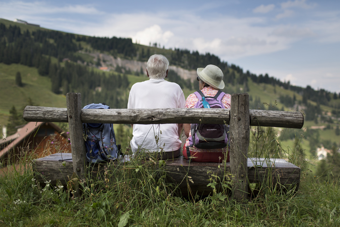 Coppia di pensionati seduti su una panchina in montagna.