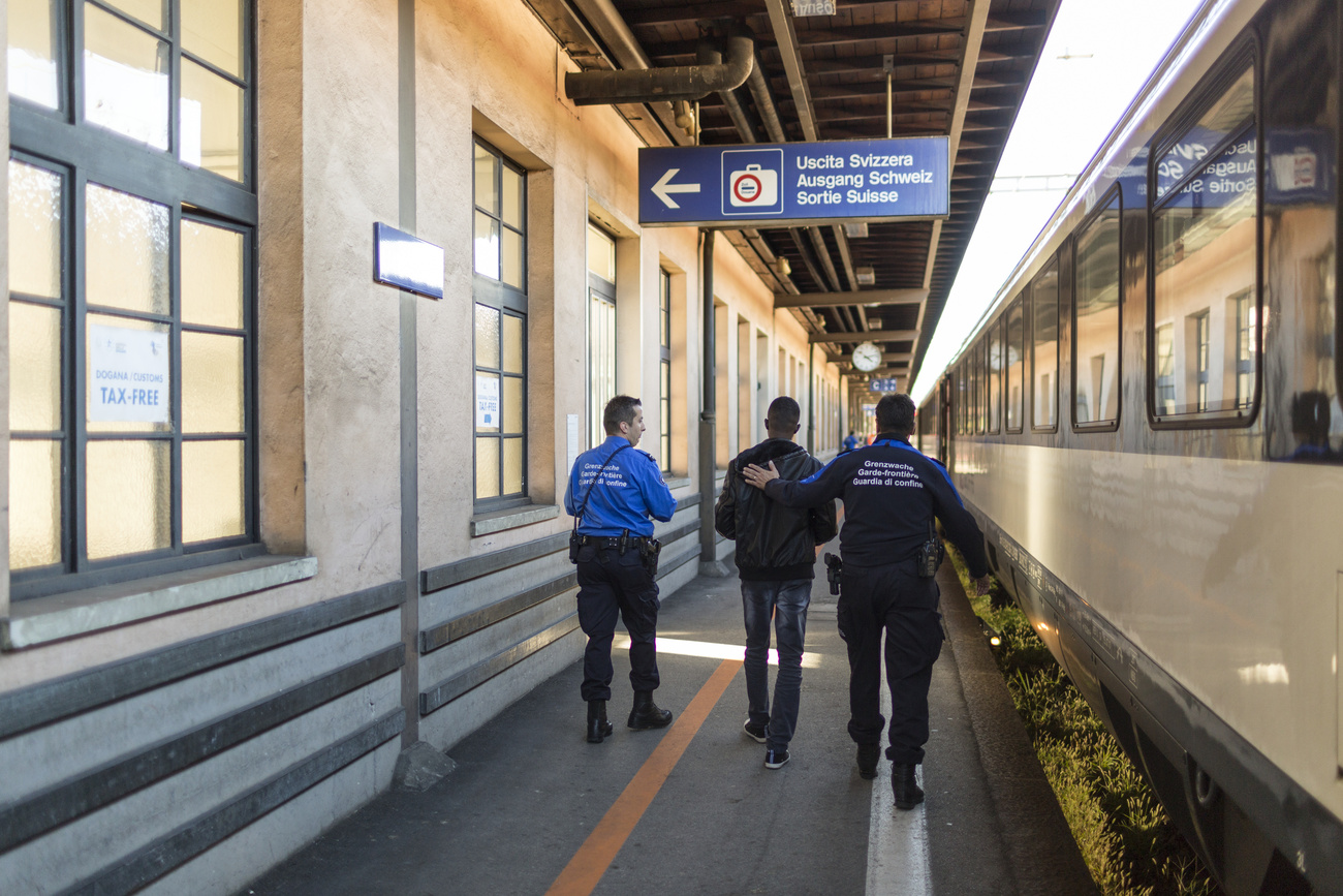 Members of the Swiss Border Guard Corps accompany an asylum seeker who entered Switzerland by train without papers to take his personal data and to question him about his reasons of entry, captured at the train station at the Swiss-Italian border in Chiasso, Switzerland, on October 23, 2014. (KEYSTONE/Gaetan Bally)