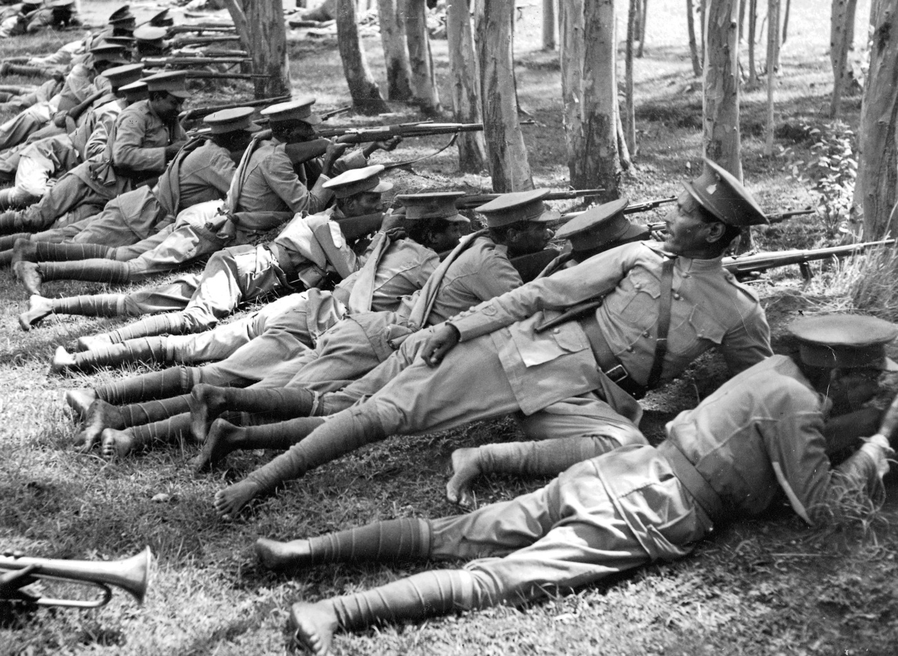 Foto in bianco e nero di soldati in uniforme a piedi nudi, distesi sull'erba mentre puntano i fucili