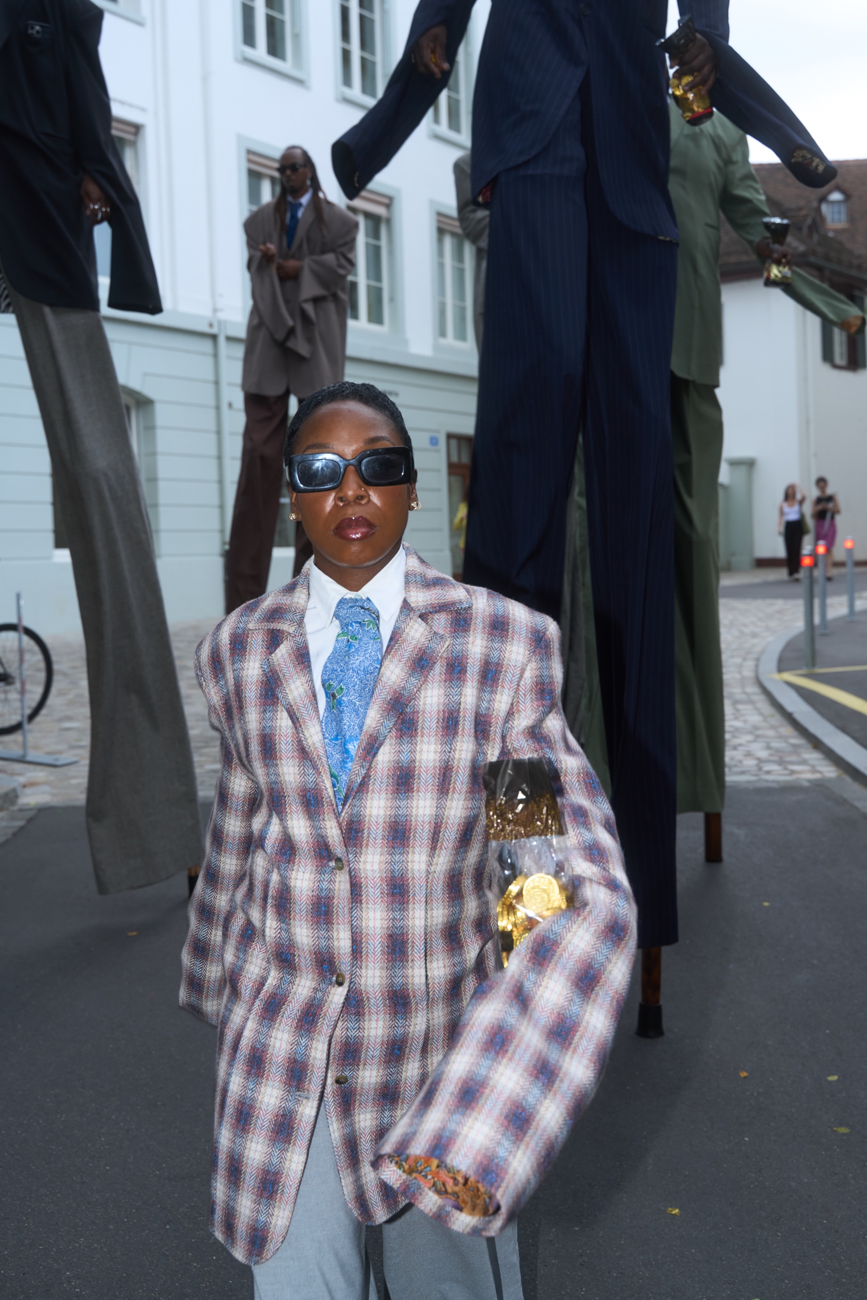 Basel Social Club year 4, "Bank" (2025): Model walks performatively by the "Bank" grounds wearing a suit designed in the same model as the sculptures in the back by Mexican artist Laura Anderson Barbata.