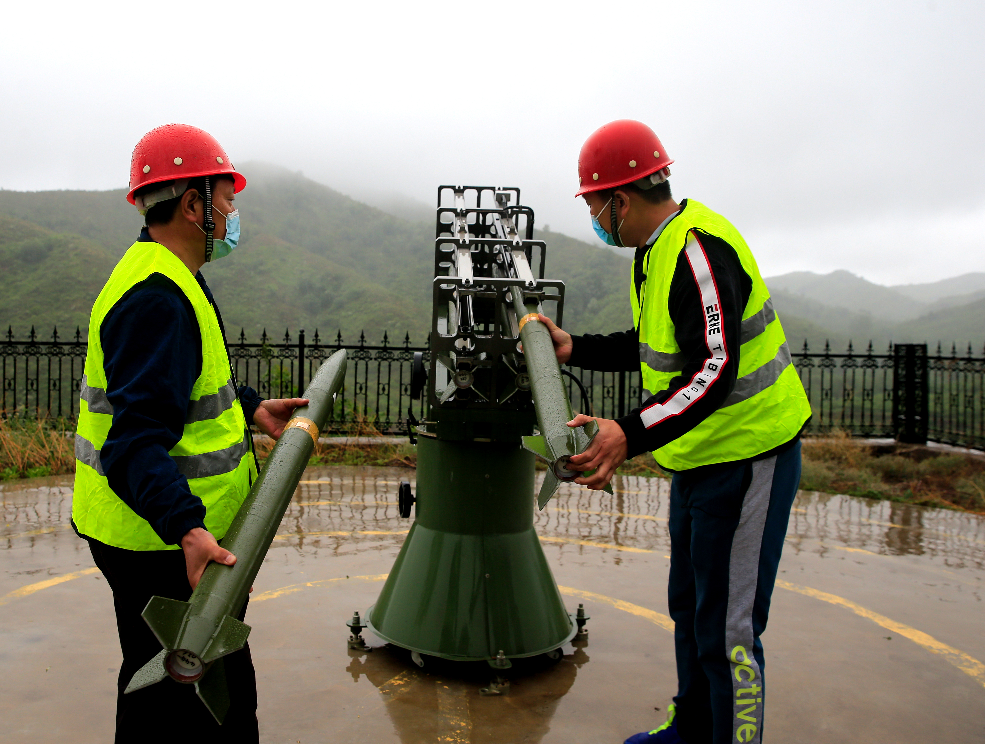 Two men are preparing rockets for cloud seeding in order to induce rain