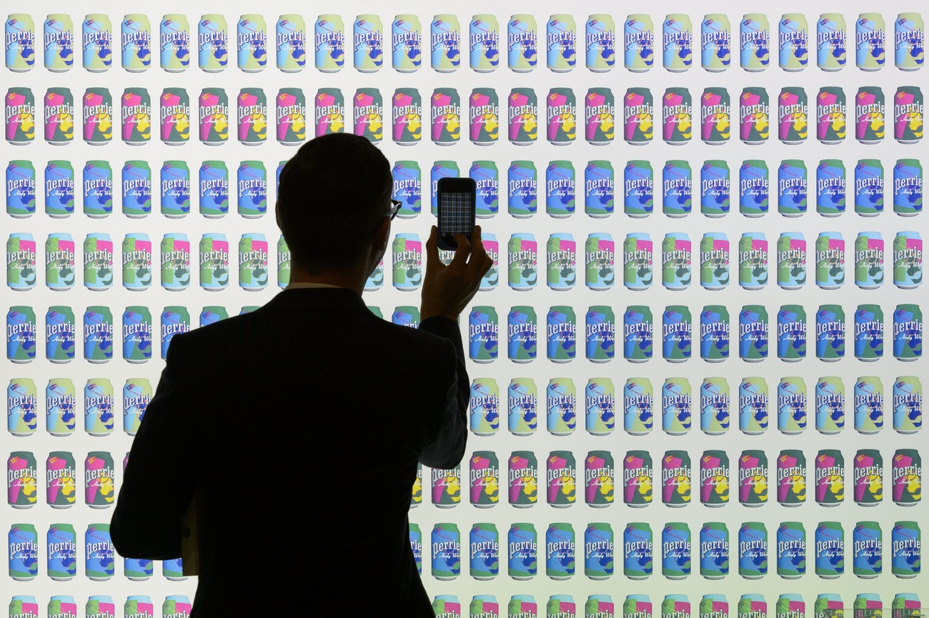 uomo fotografa muro con centinaia di immagini di lattine di acqua perrier