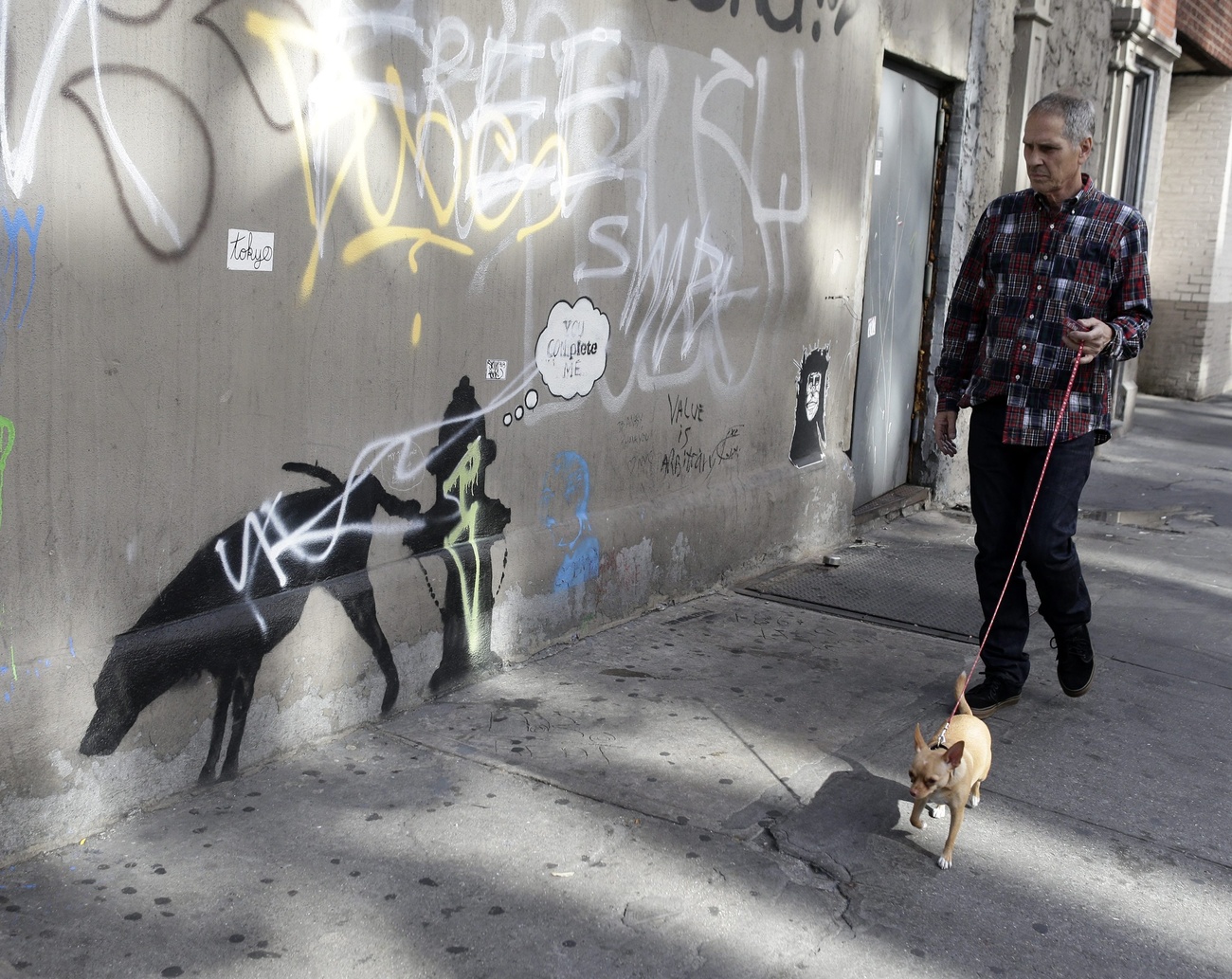 uomo con cane al guinzaglio passa accanto a graffito di banksy di un cane che fa la pipì contro un idrante