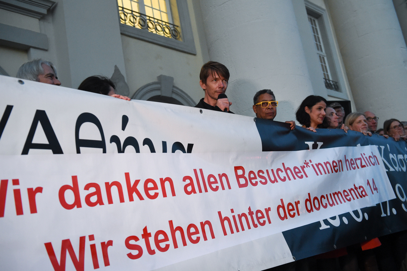 Adam Szymczyk (centre) speaks in front of a banner expressing gratitude at the close of documenta 14 in Kassel, September 2017. Besides, or because of its peculiar global prestige, the documenta also leaves its heads exposed to all sorts of criticism.