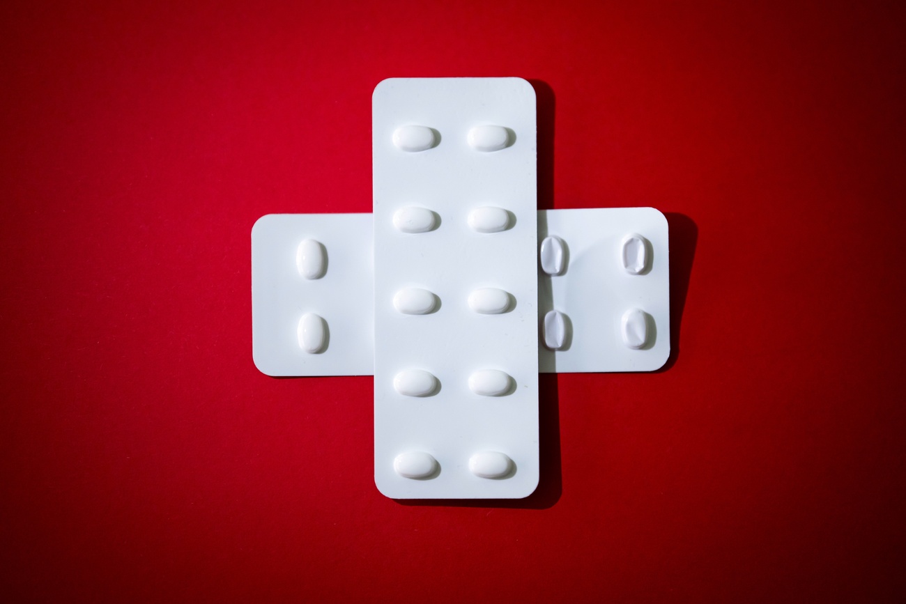 croce svizzera fatta con due blister bianchi di medicinali incrociati su sfondo rosso