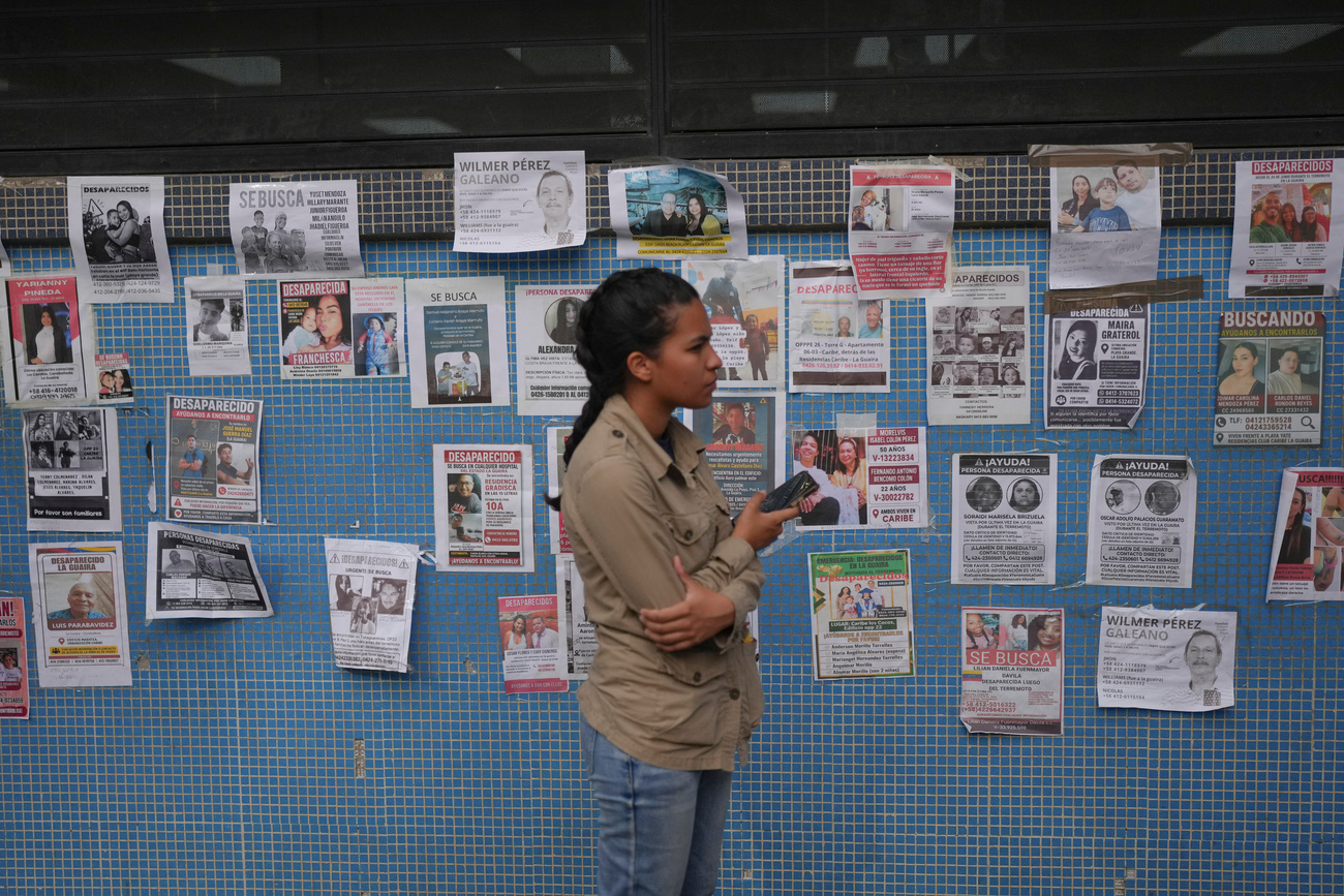 Eine Frau steht vor Plakaten mit Fotos von Vermissten