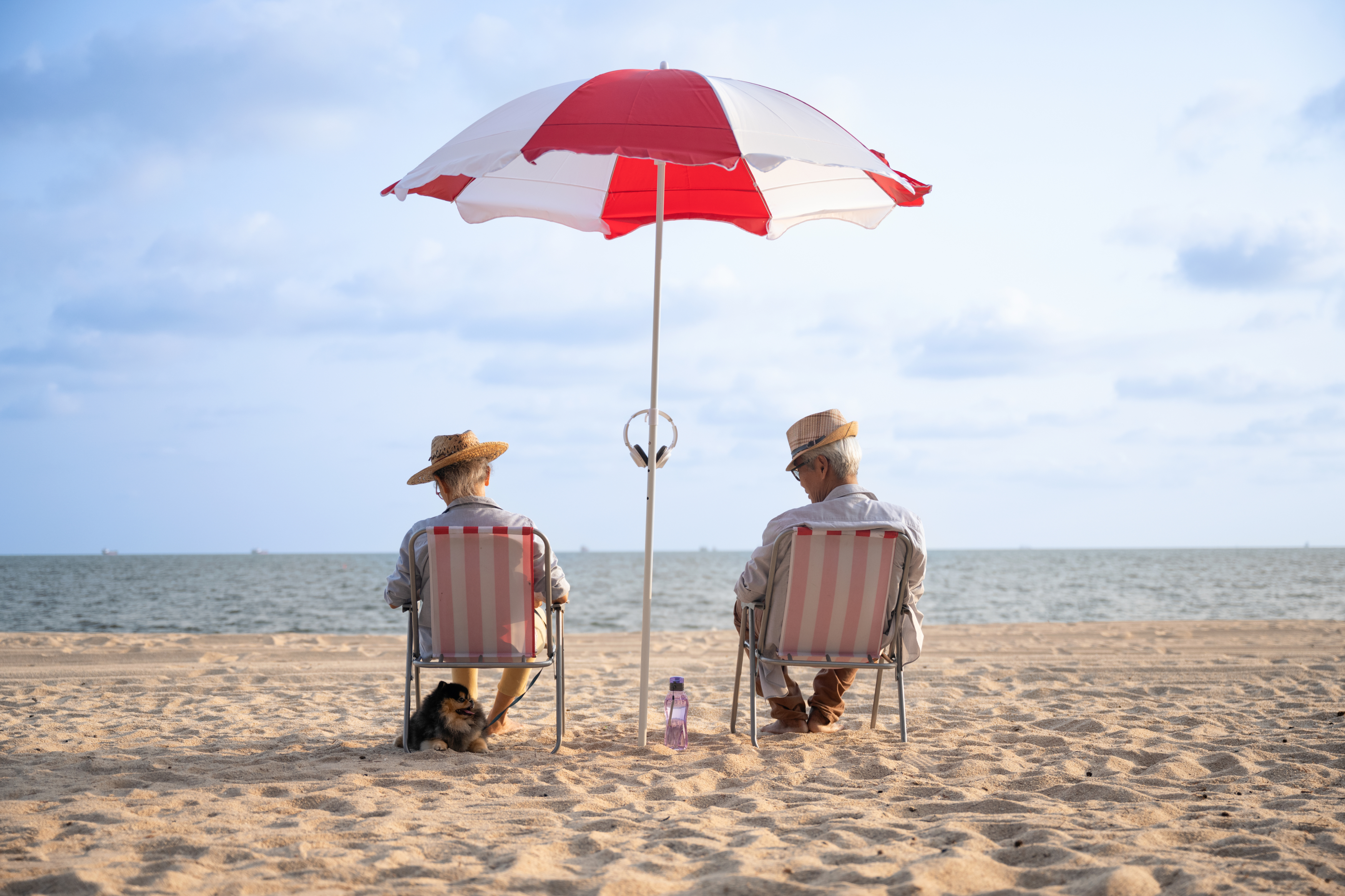 Ein altes Paar sitzt auf Stühlen unter einem Sonnenschirm an einem Strand
