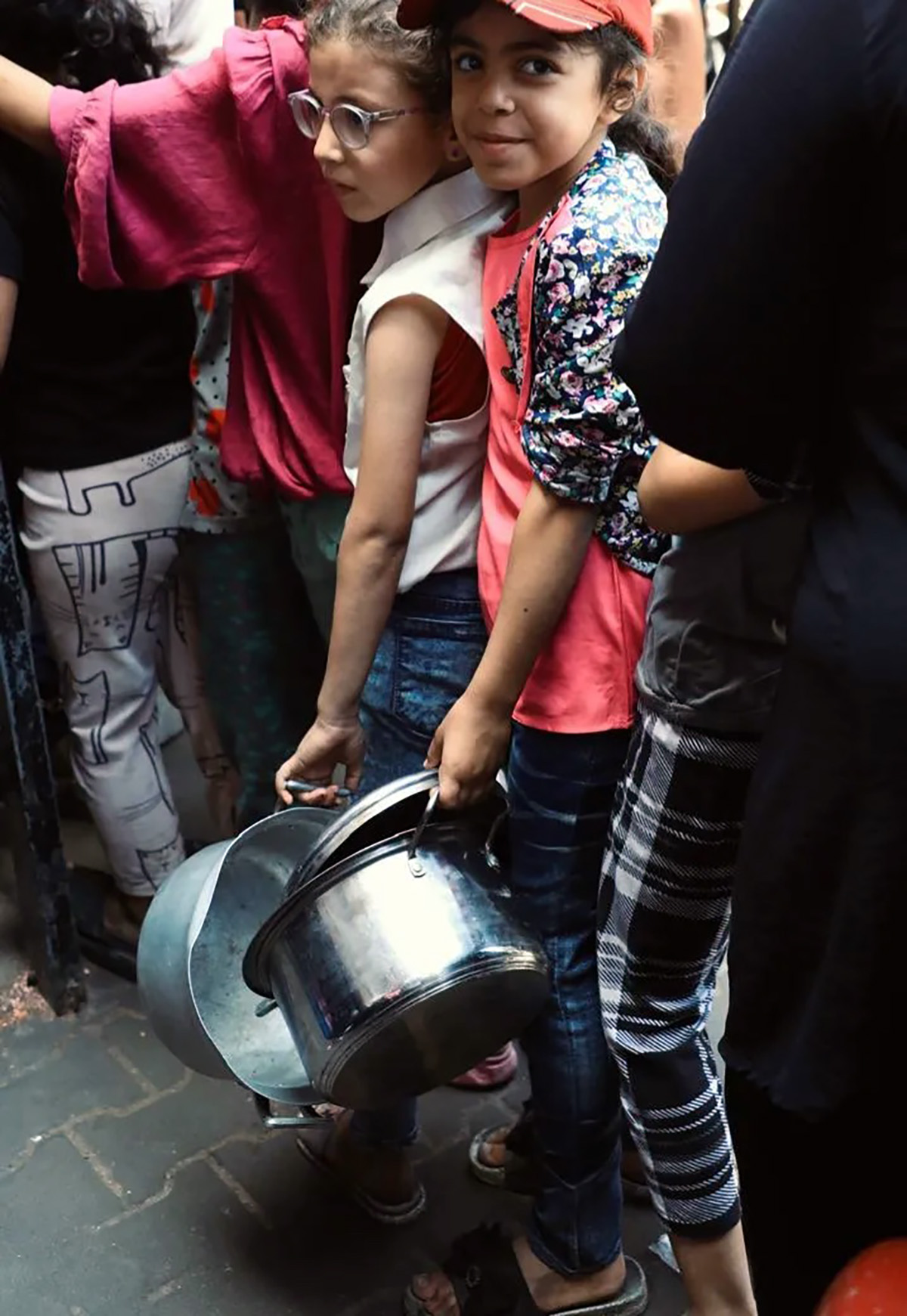 Unas niñas palestinas desplazadas llevan ollas mientras esperan frente a una «takiya», una cocina comunitaria, en Al-Mawasi, Khan Younis, al sur de Gaza.