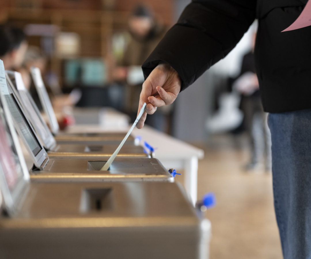 A person is putting a ballot paper into a ballot box.