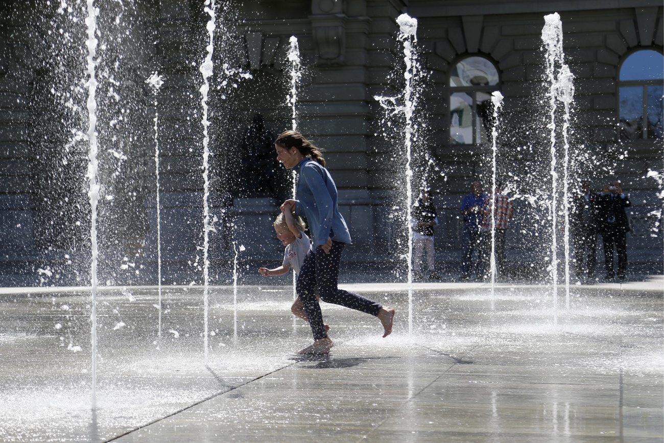 donna con bambino corrono in mezzo a getti d'acqua su piazza federale a berna