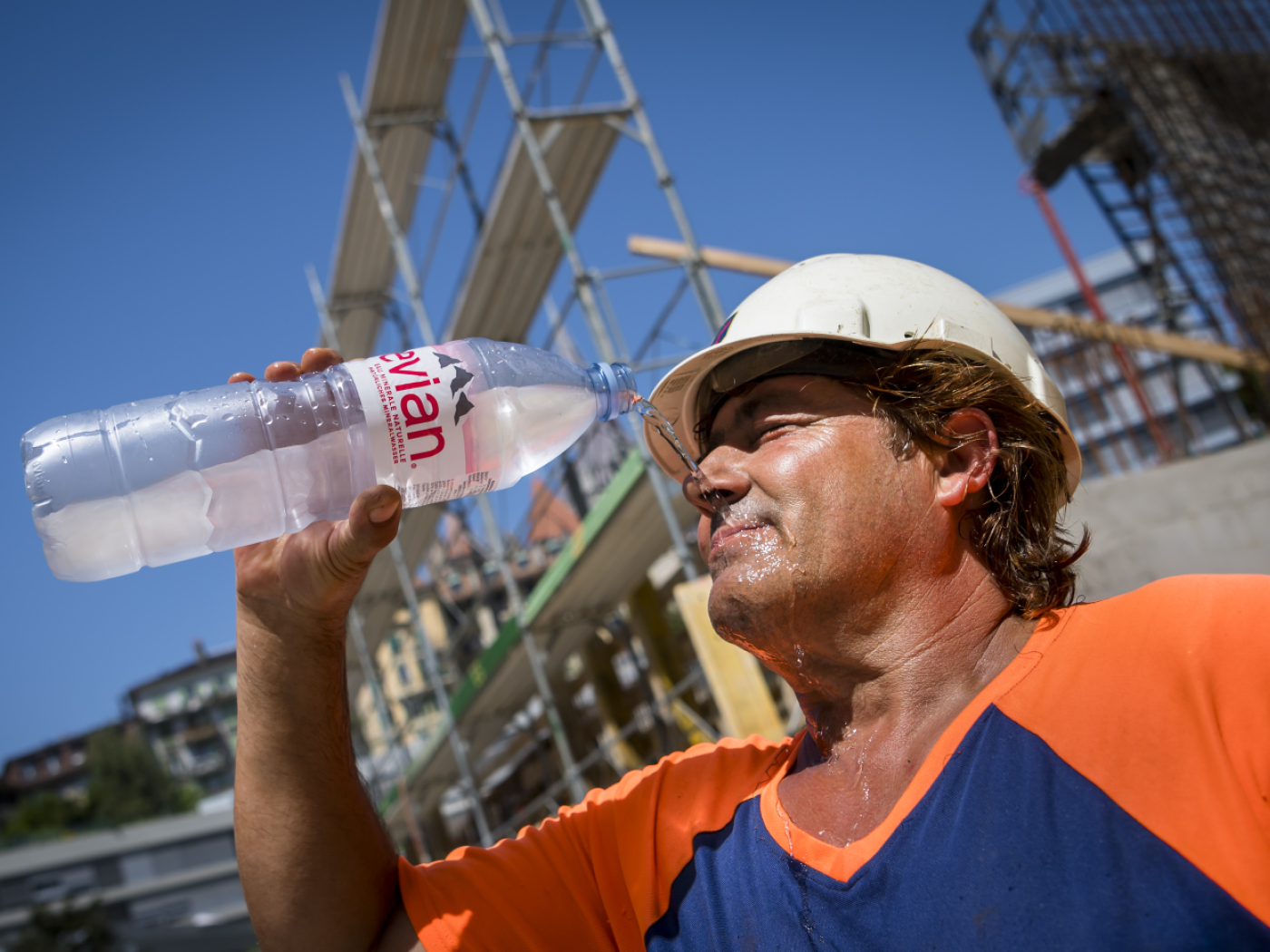 operaio di cantiere si bagna il viso con una bottiglia di acqua evian