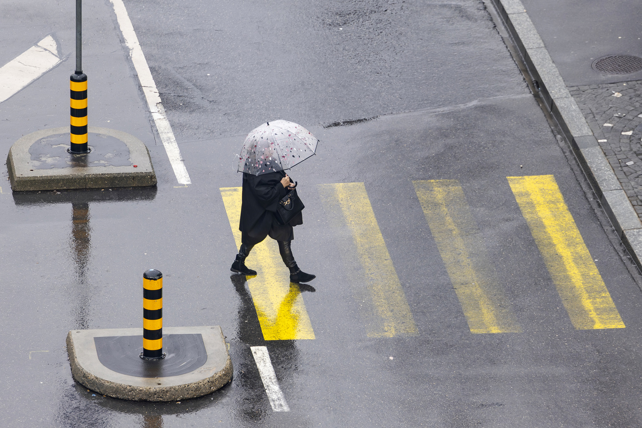 une femme traverse un passage piéton sous la pluie