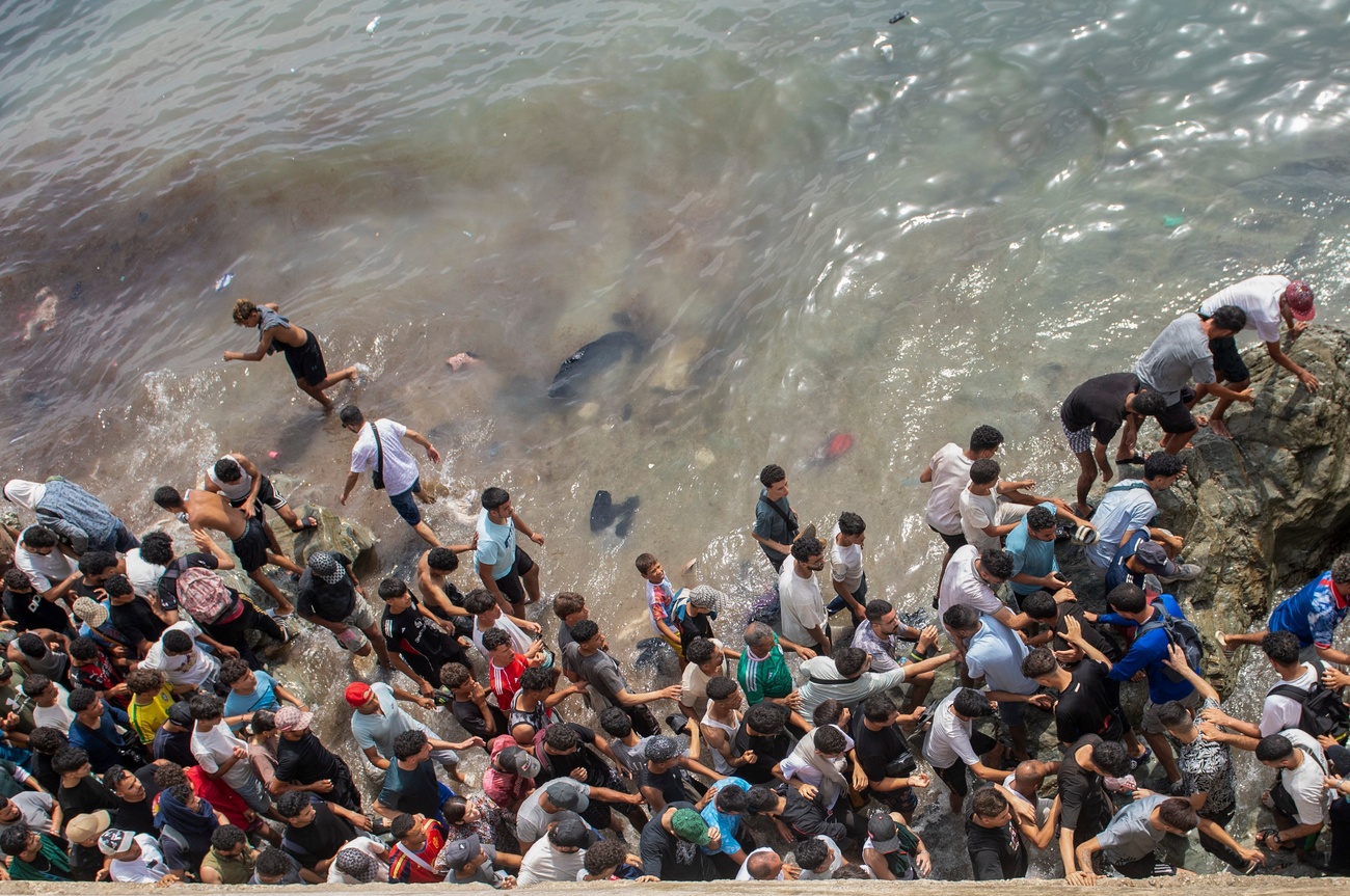 Viele Menschen drängen sich an einem Strand, den sie in Kleidern schwimmend erreicht haben
