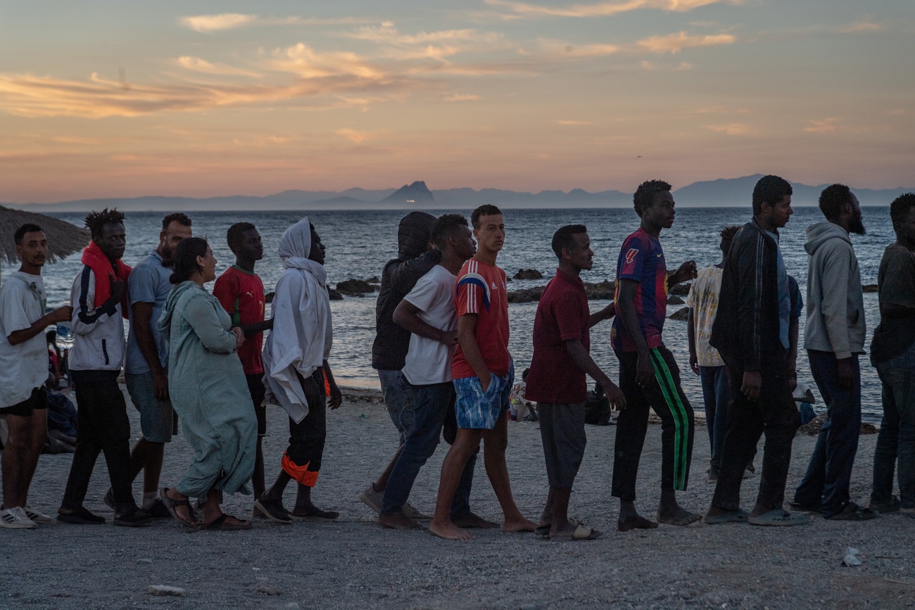 Migrantinnen und Migranten stehen an einem Strand für die Essensverteilung an
