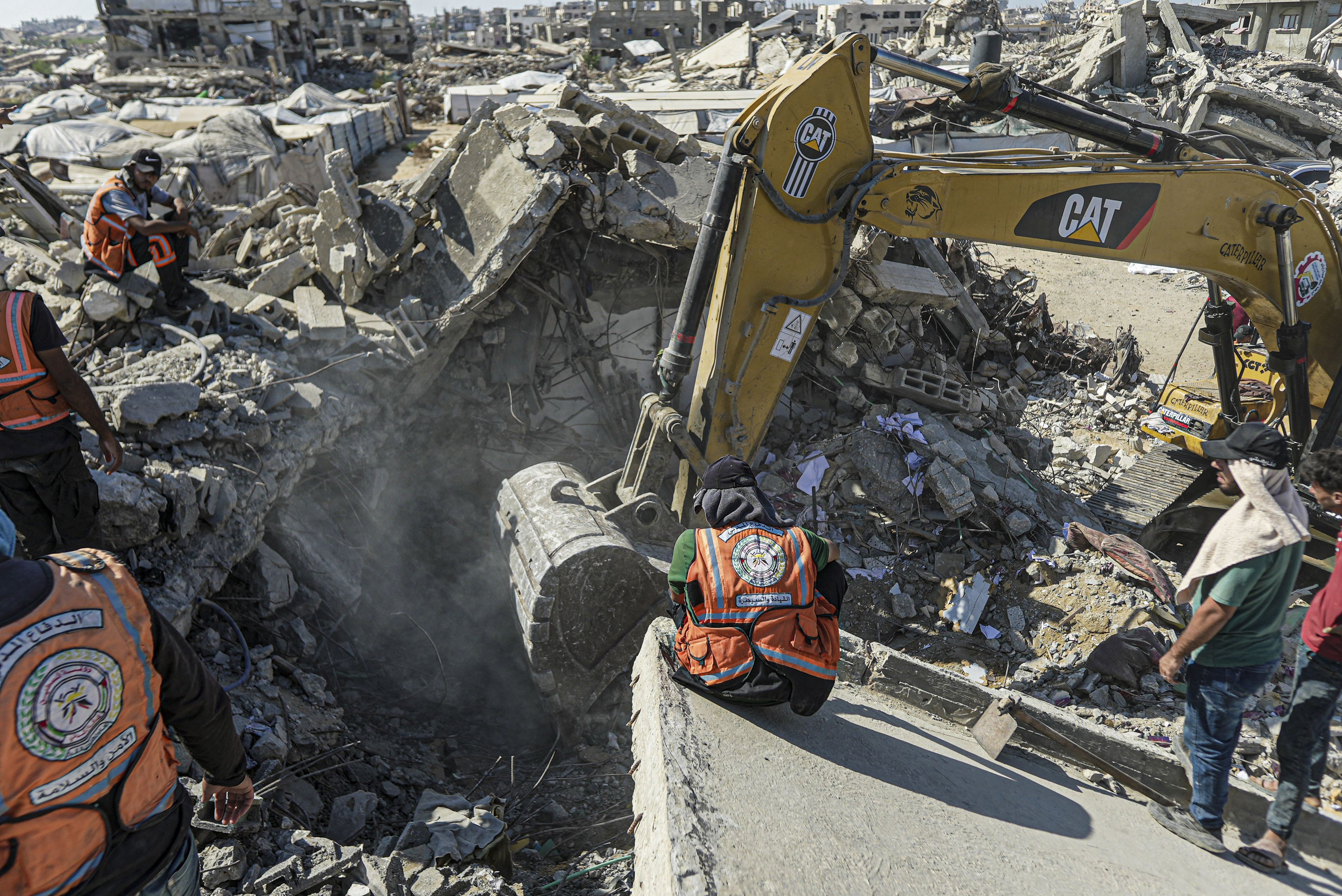 An excavator clears rubble as Palestinian Civil Defense crews and residents look on in the Zeitoun neighborhood of Gaza City