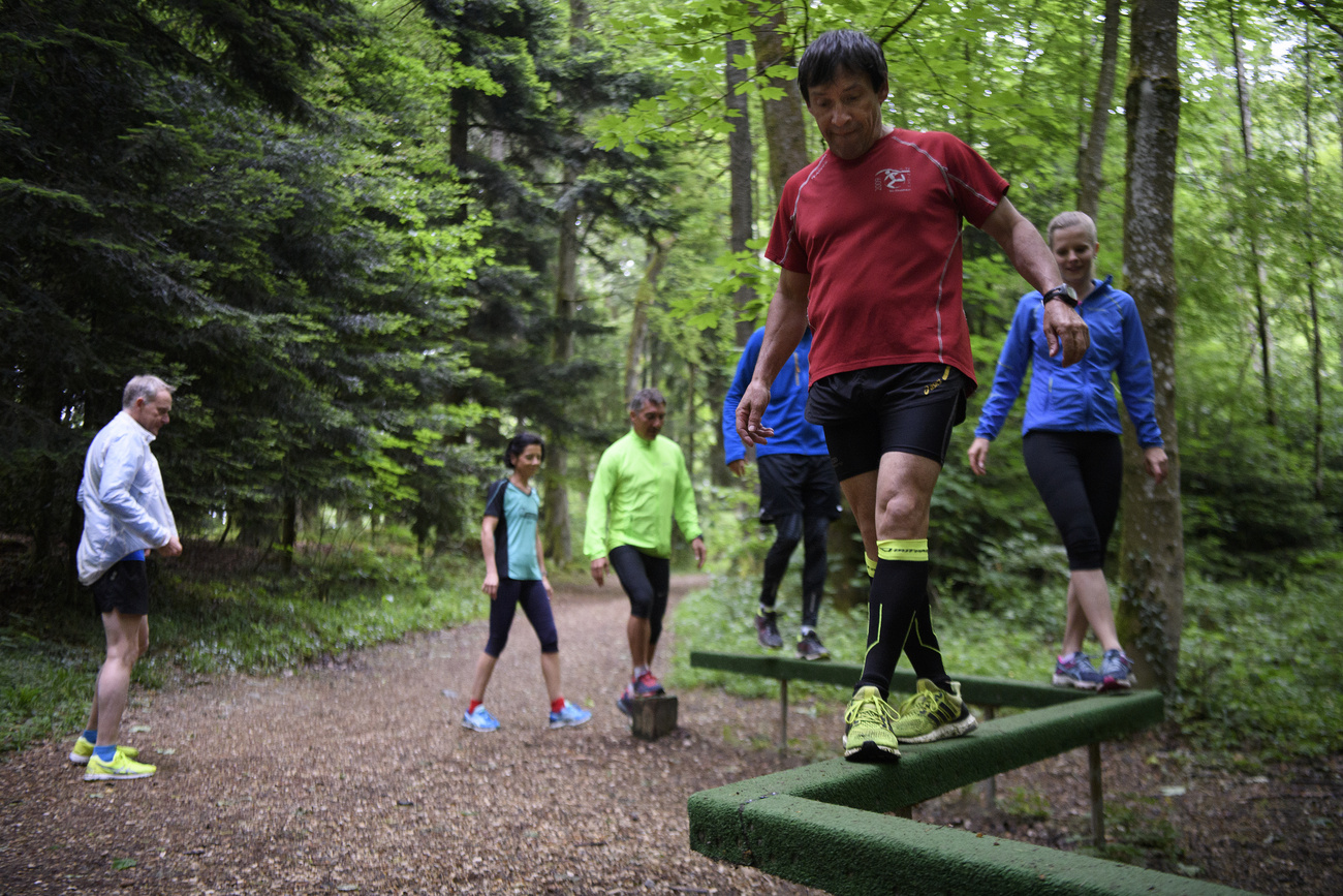 Plusieurs personnes marchent en équilibre sur les poutres en bois d'un parcours de santé.