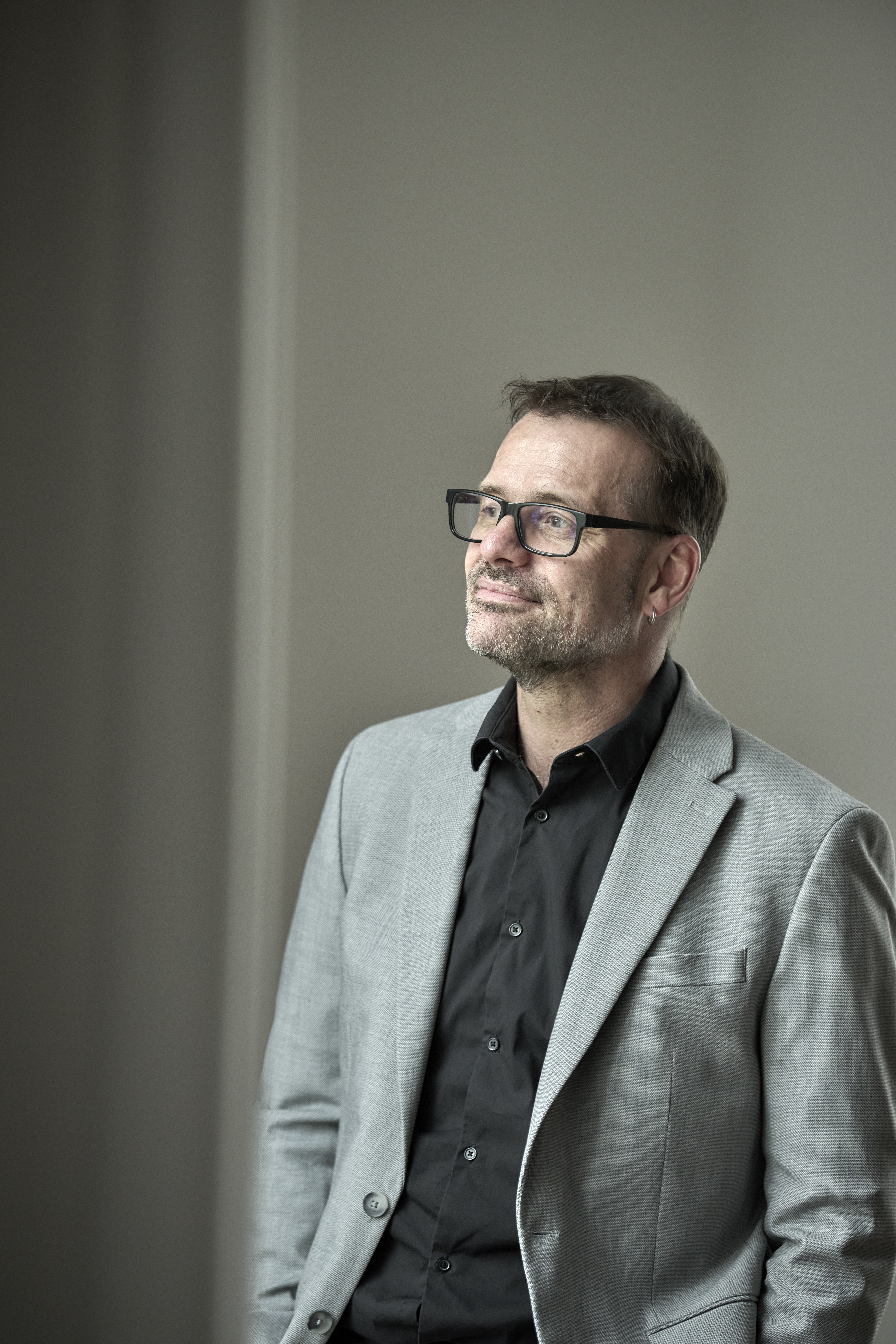 un homme brun en costume gris avec des lunettes