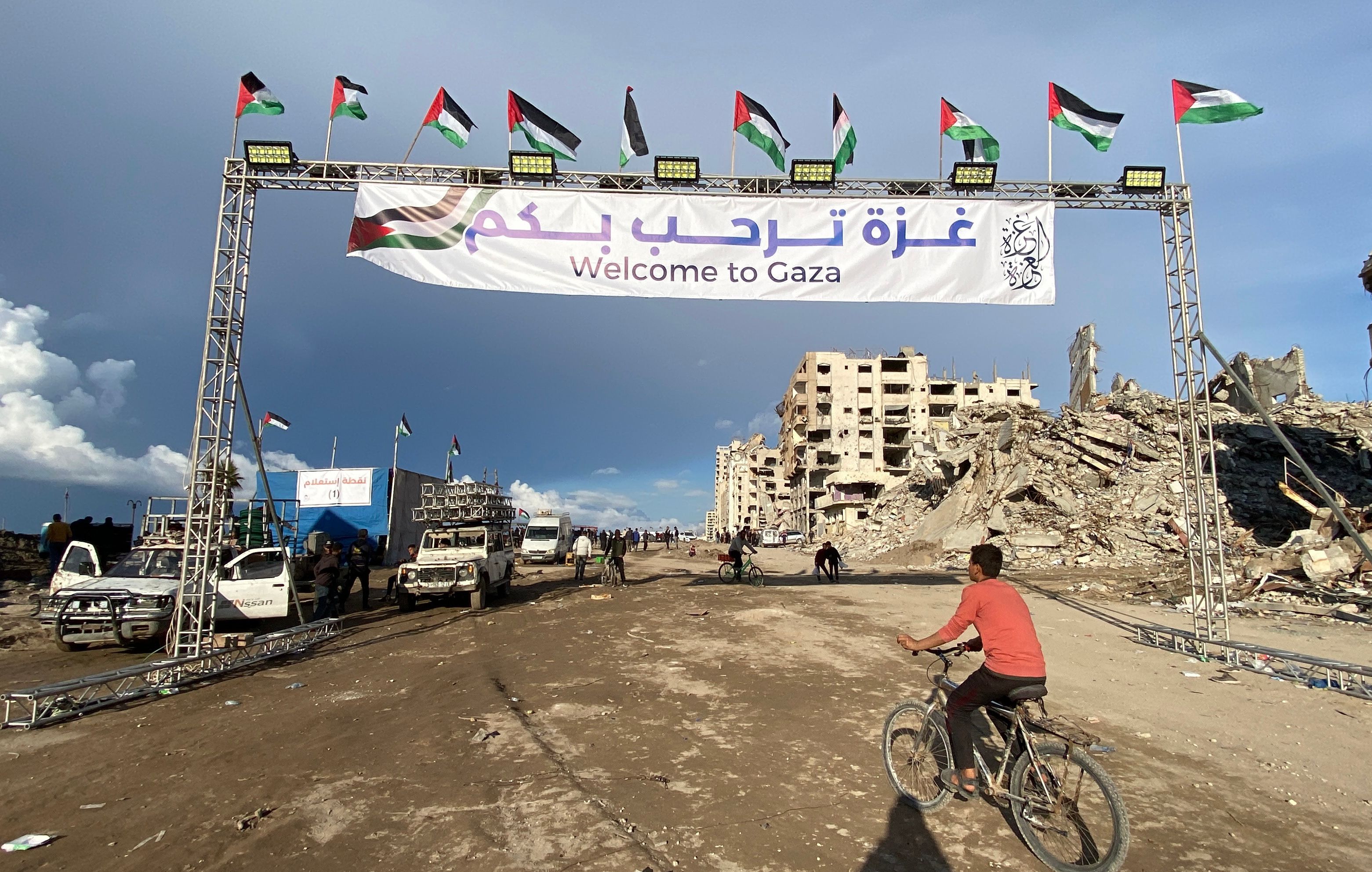 People gather by a banner welcoming people near the rubble of a collapsed building along Gaza's coastal al-Rashid Street for people to cross from the Israeli-blocked Netzarim corridor from the southern Gaza Strip into Gaza City on January 26, 2025.