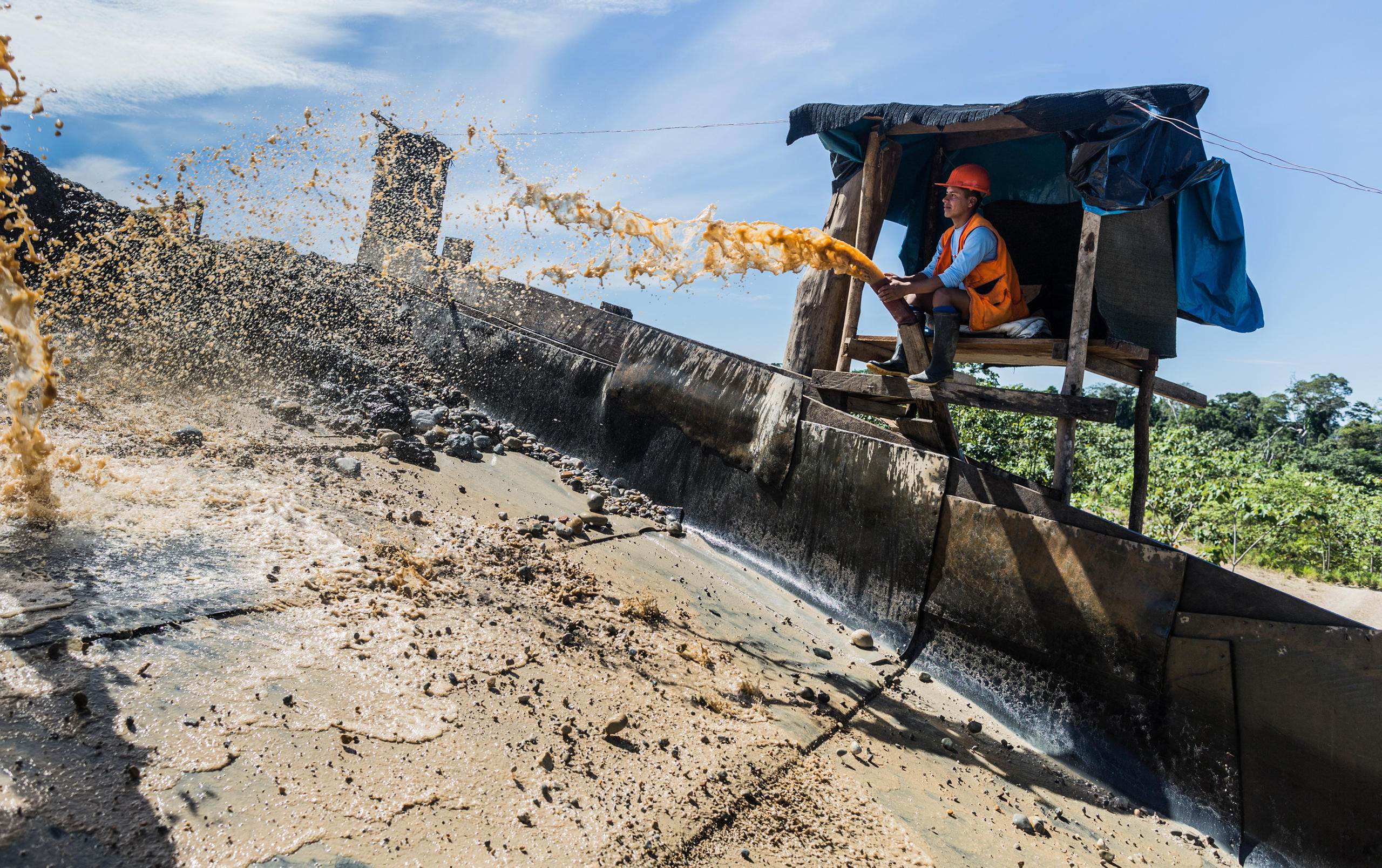 A worker at a chute in Juan Ttamin's mine. As ore is emptied from a truck onto the chute, water separates the gold from other matter. The precious metal is then caught in a mat below.